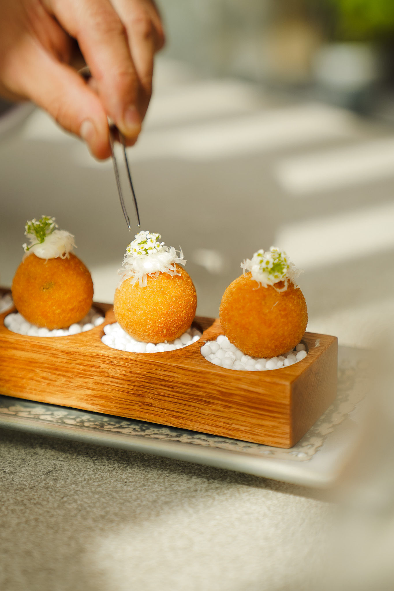 Gourmet fried appetizers on wood tray, chef garnishing with white flowers.
