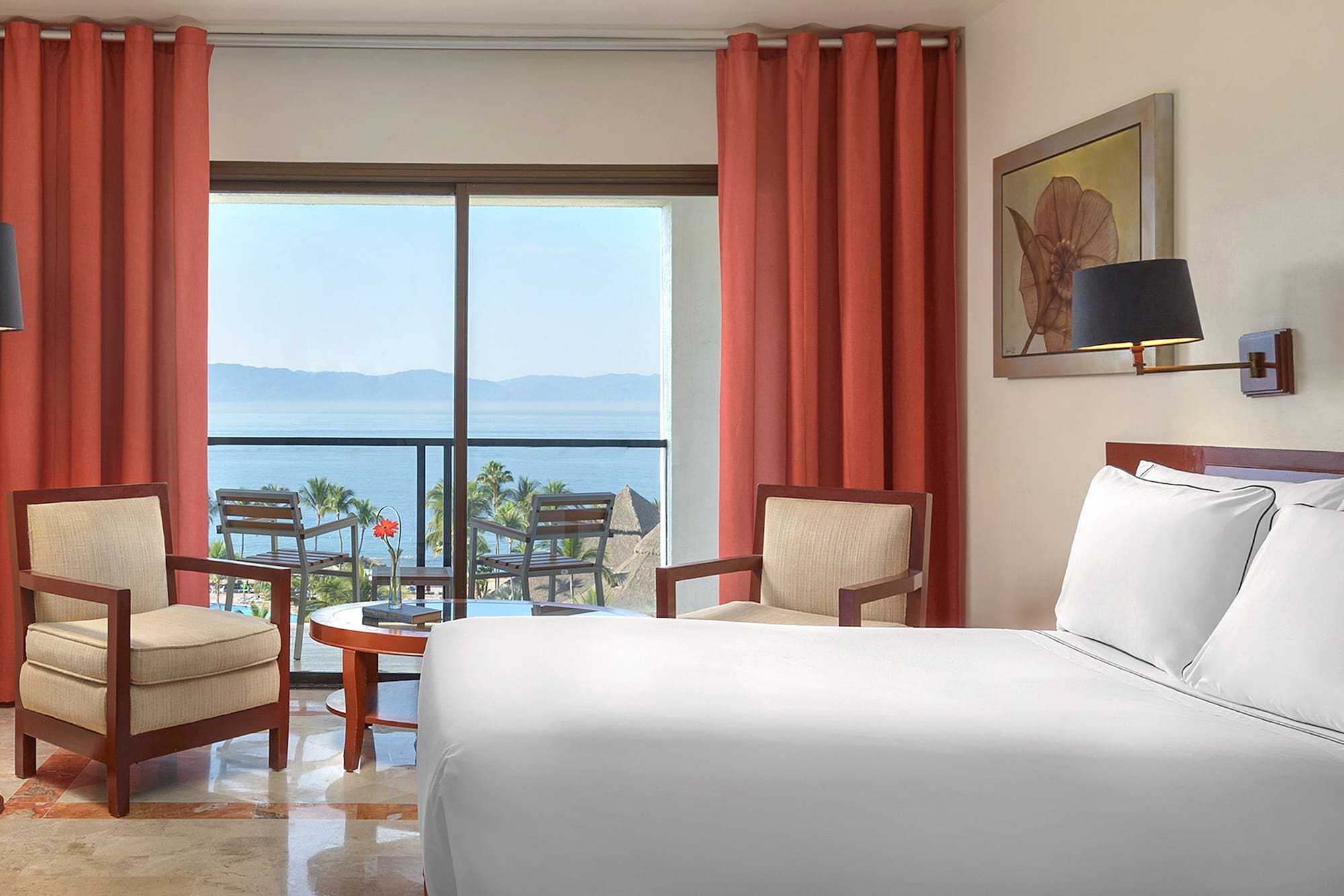 a room with a bed and chairs and a table with chairs and a view of the ocean