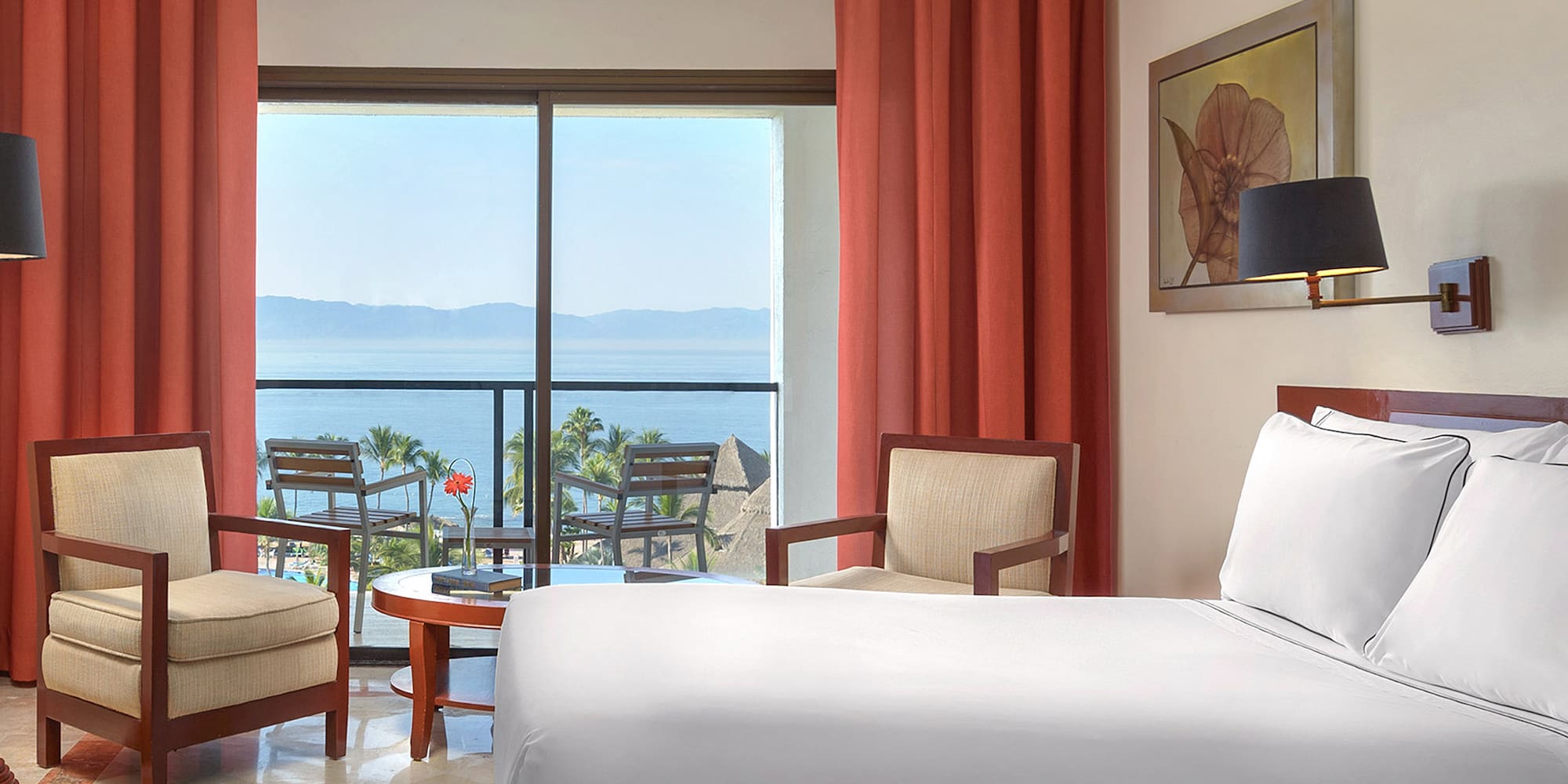 a room with a bed and chairs and a table with chairs and a view of the ocean