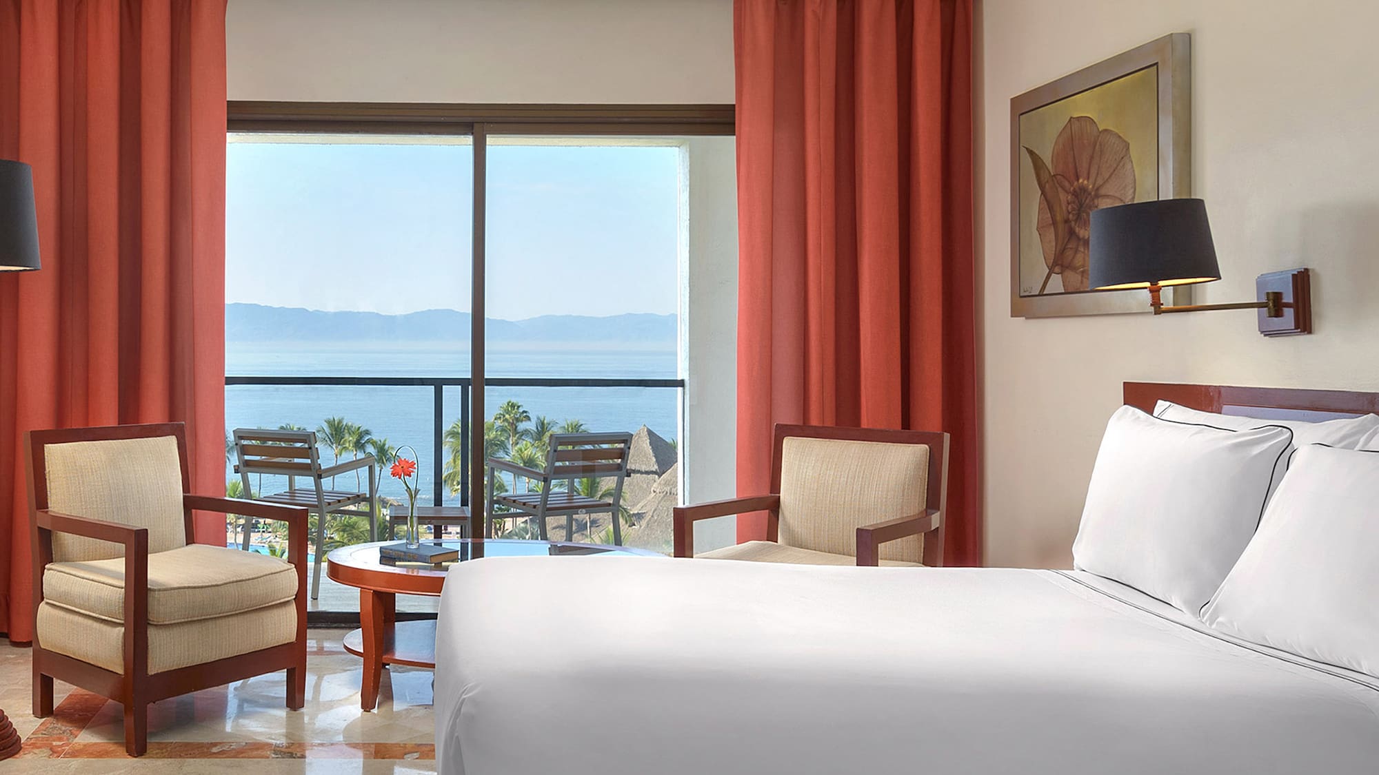 a room with a bed and chairs and a table with chairs and a view of the ocean