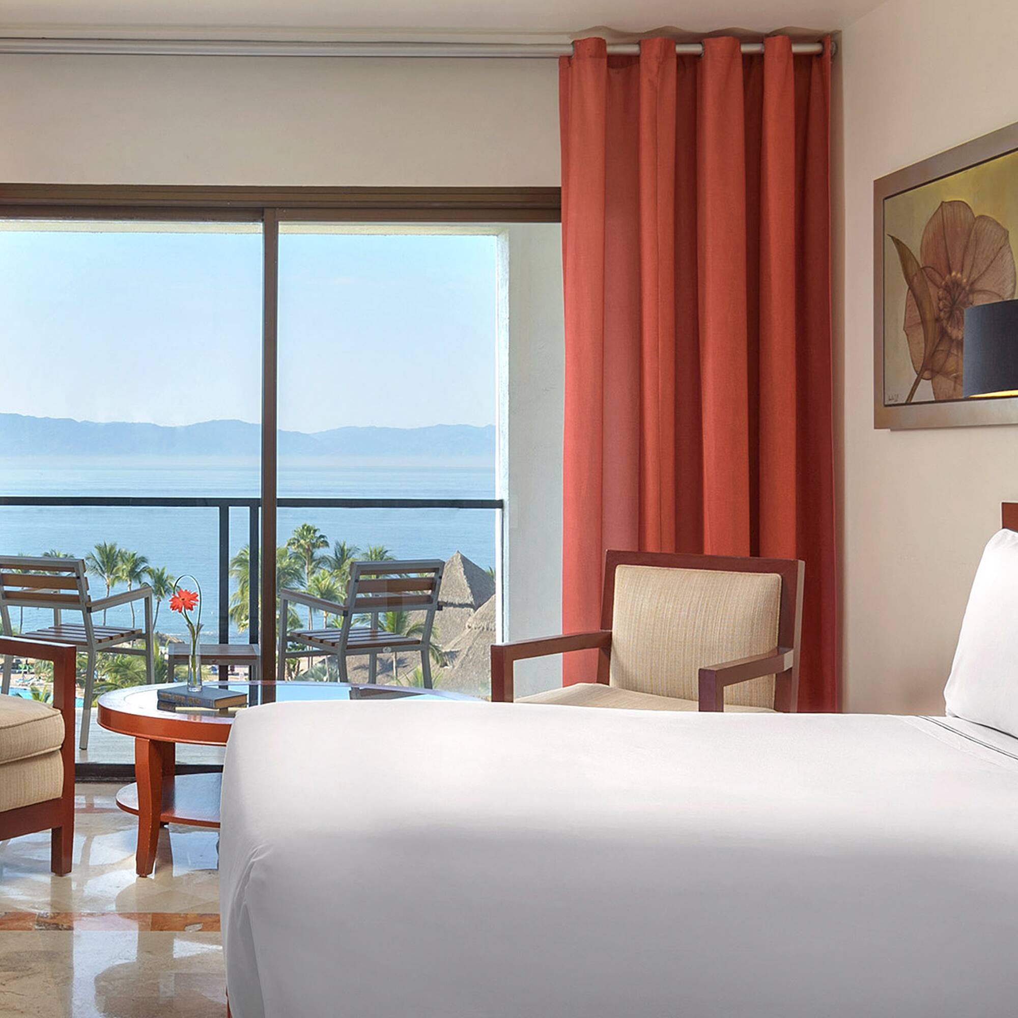 a room with a bed and chairs and a table with chairs and a view of the ocean