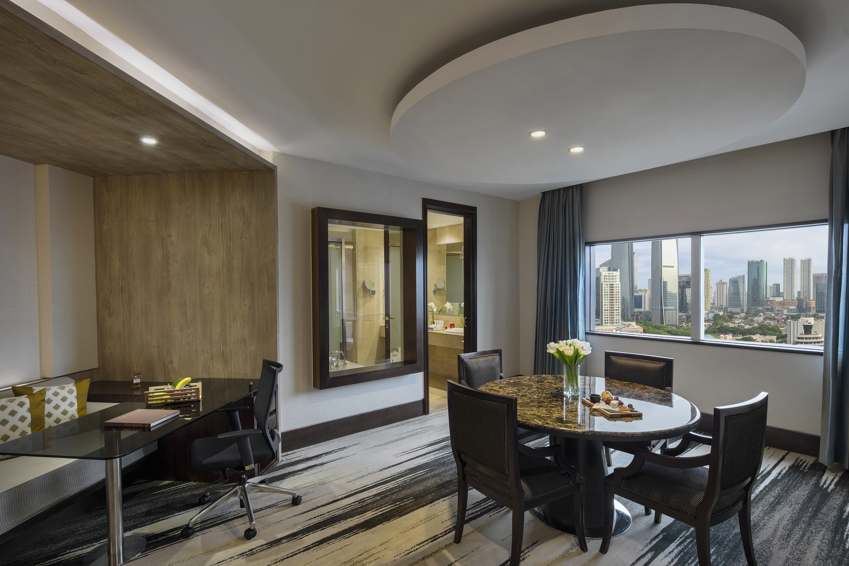 Luxury hotel suite with city skyline view, dining, and work areas.