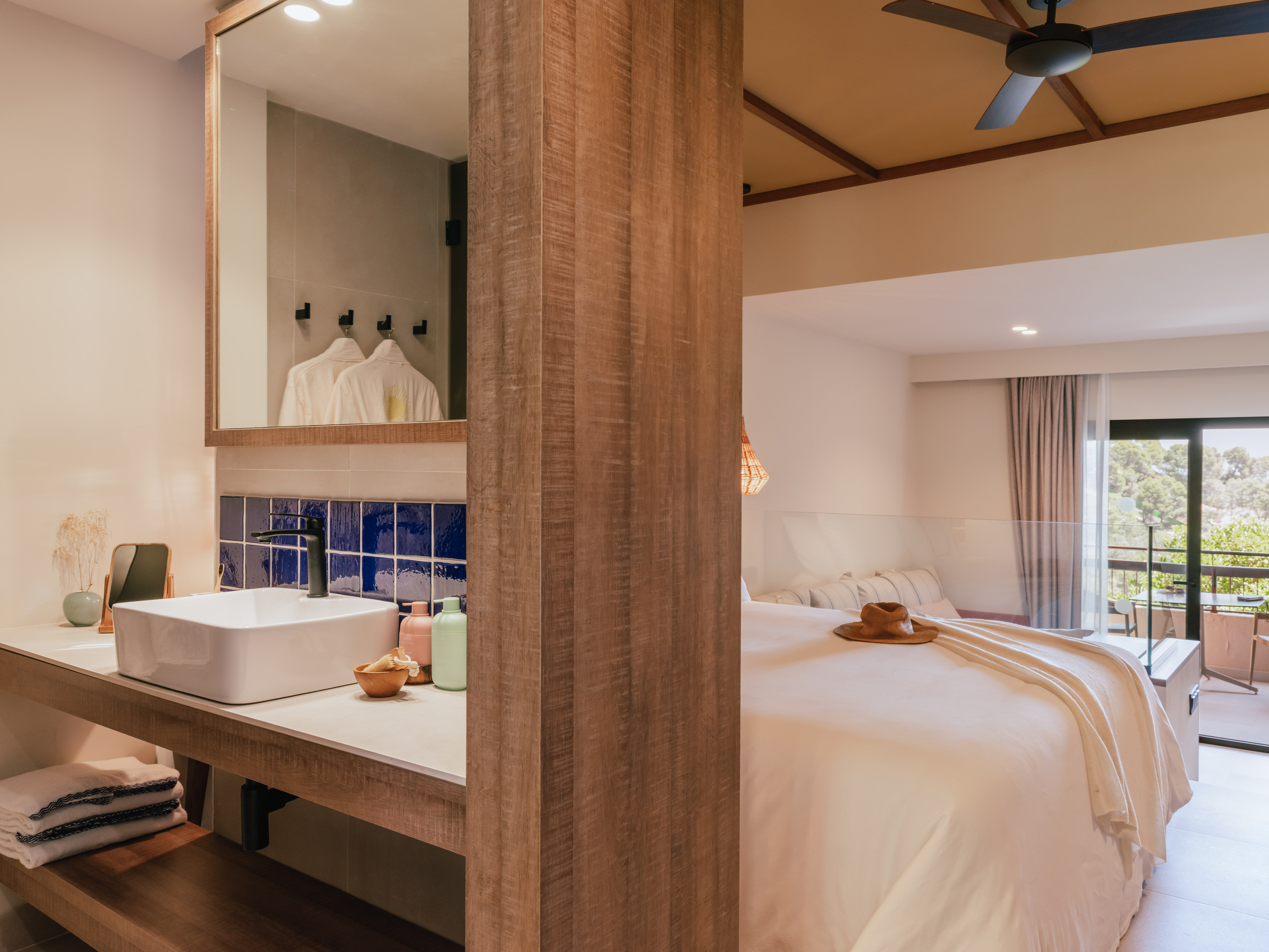 Modern hotel suite with open bathroom, large bed, and balcony view.