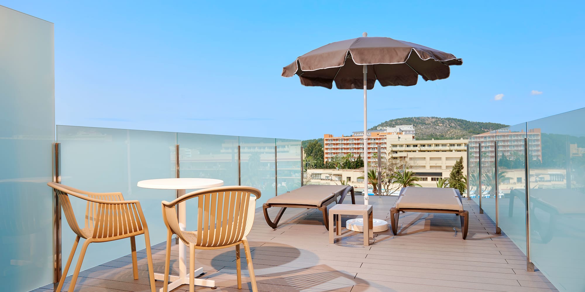 Modern rooftop terrace with lounge chairs, umbrella, and glass railing.