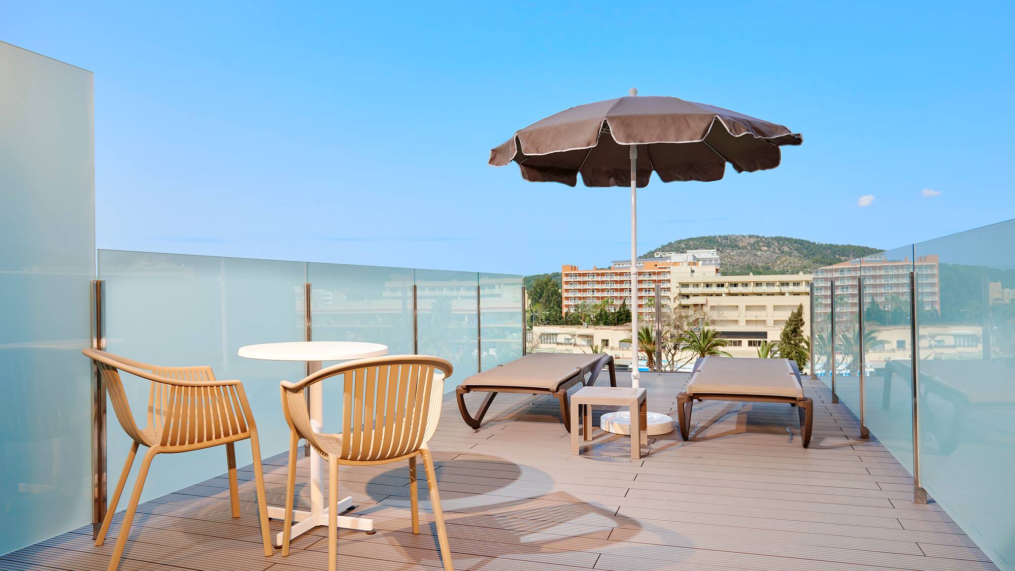 Modern rooftop terrace with lounge chairs, umbrella, and glass railing.