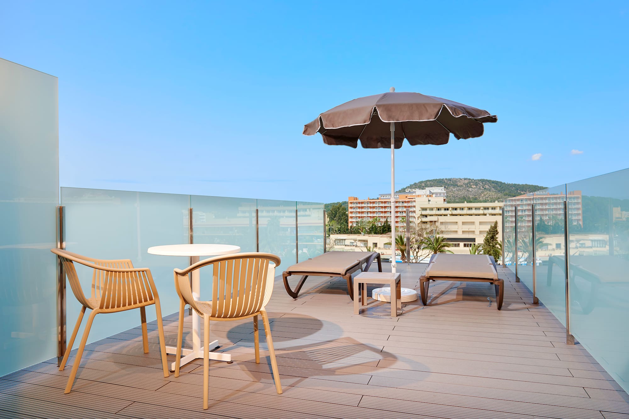 Modern rooftop terrace with lounge chairs, umbrella, and glass railing.