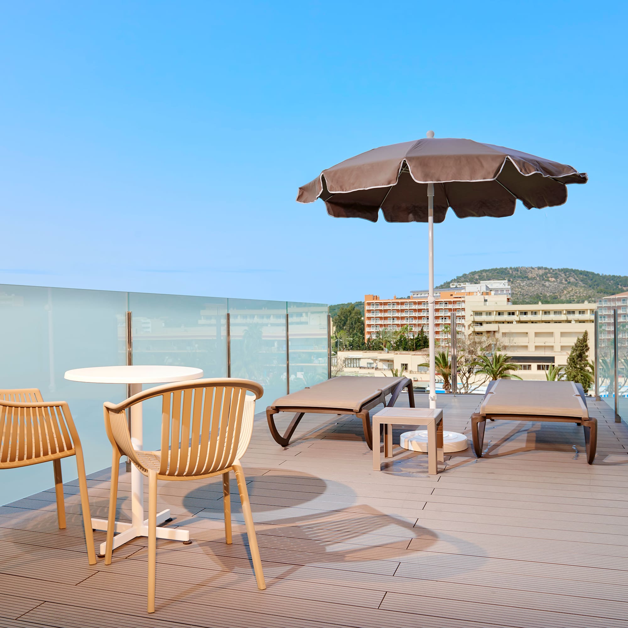 Modern rooftop terrace with lounge chairs, umbrella, and glass railing.