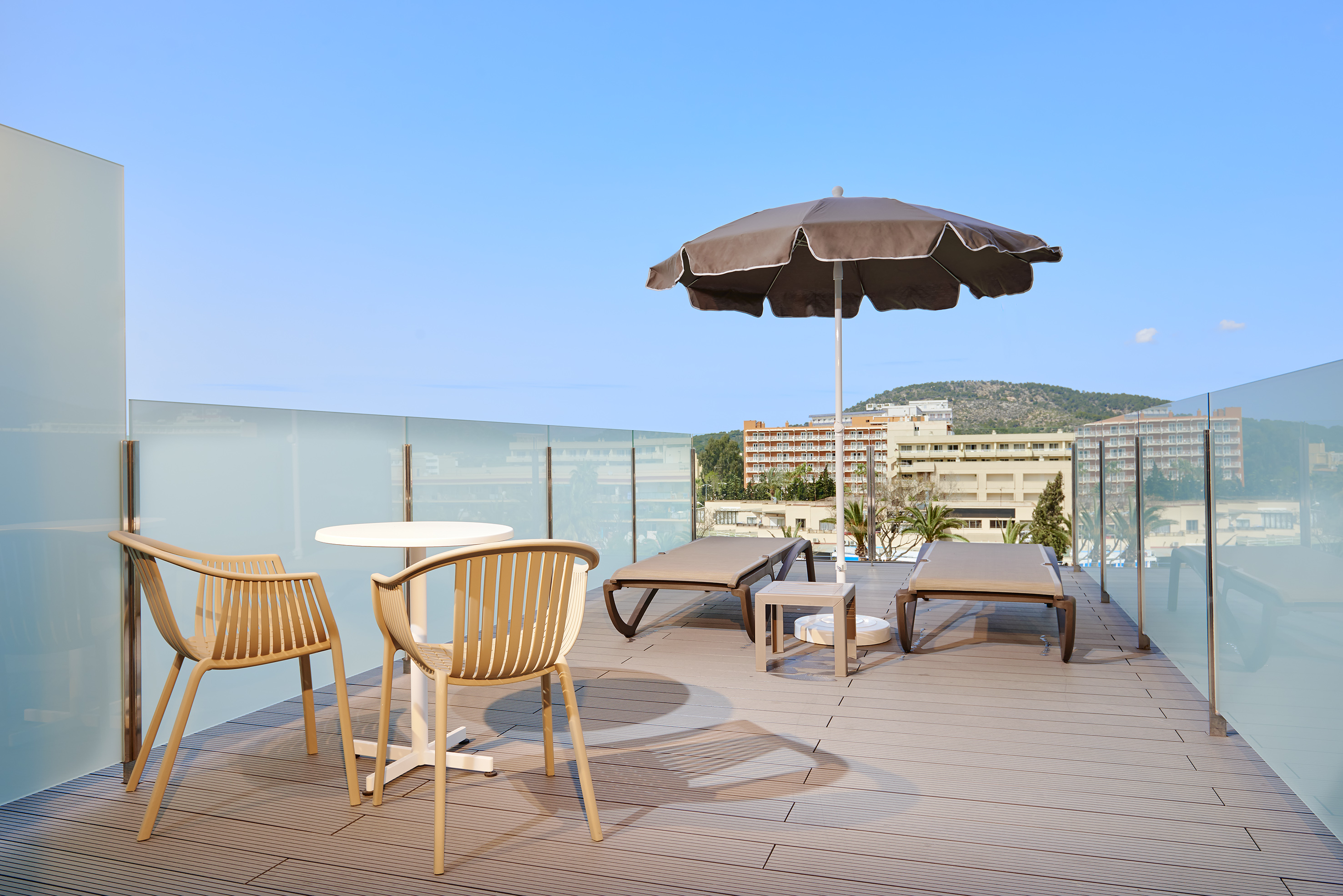 Modern rooftop terrace with lounge chairs, umbrella, and glass railing.