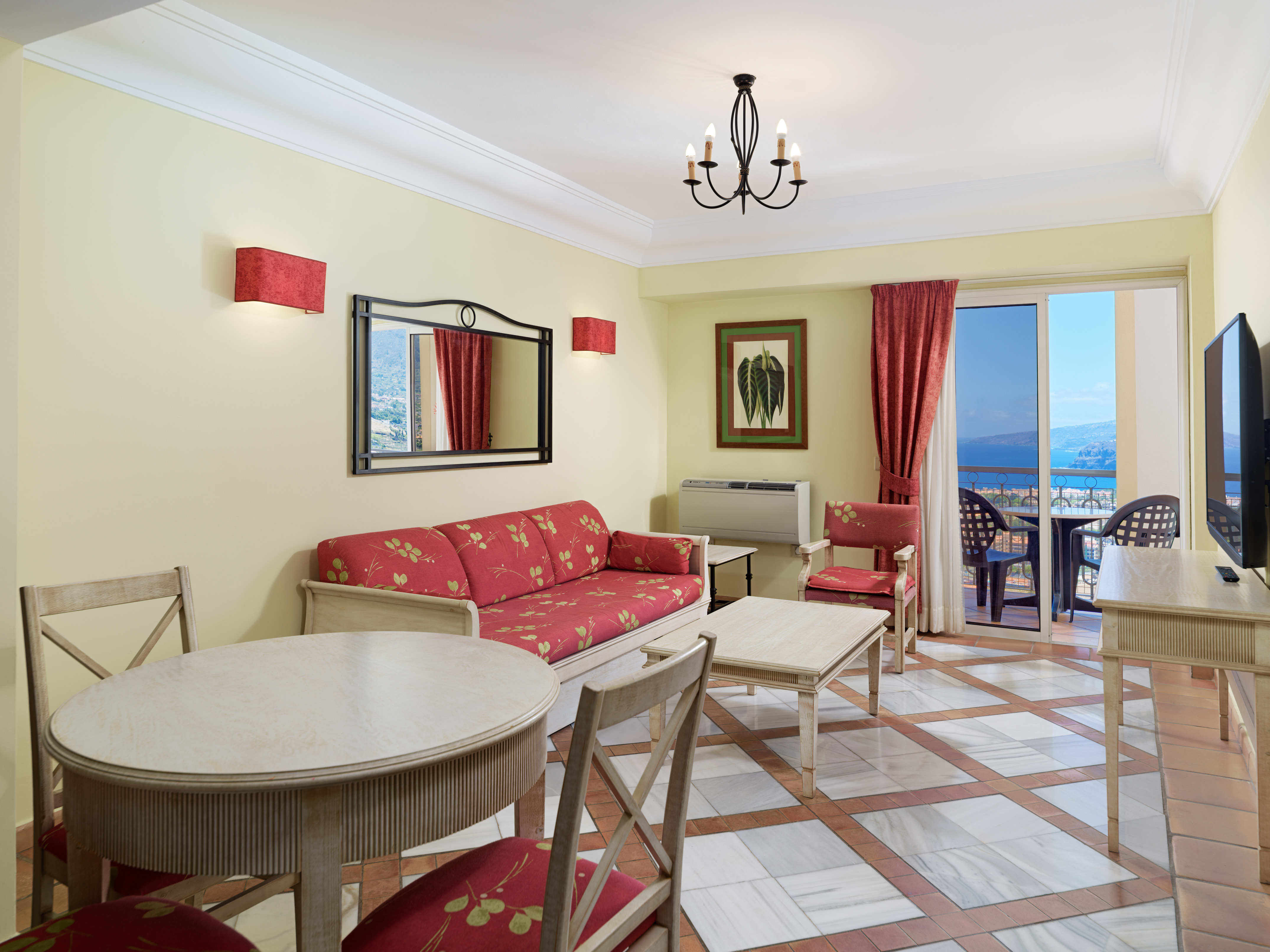 Hotel suite living room with red sofa, dining, and sea view balcony.