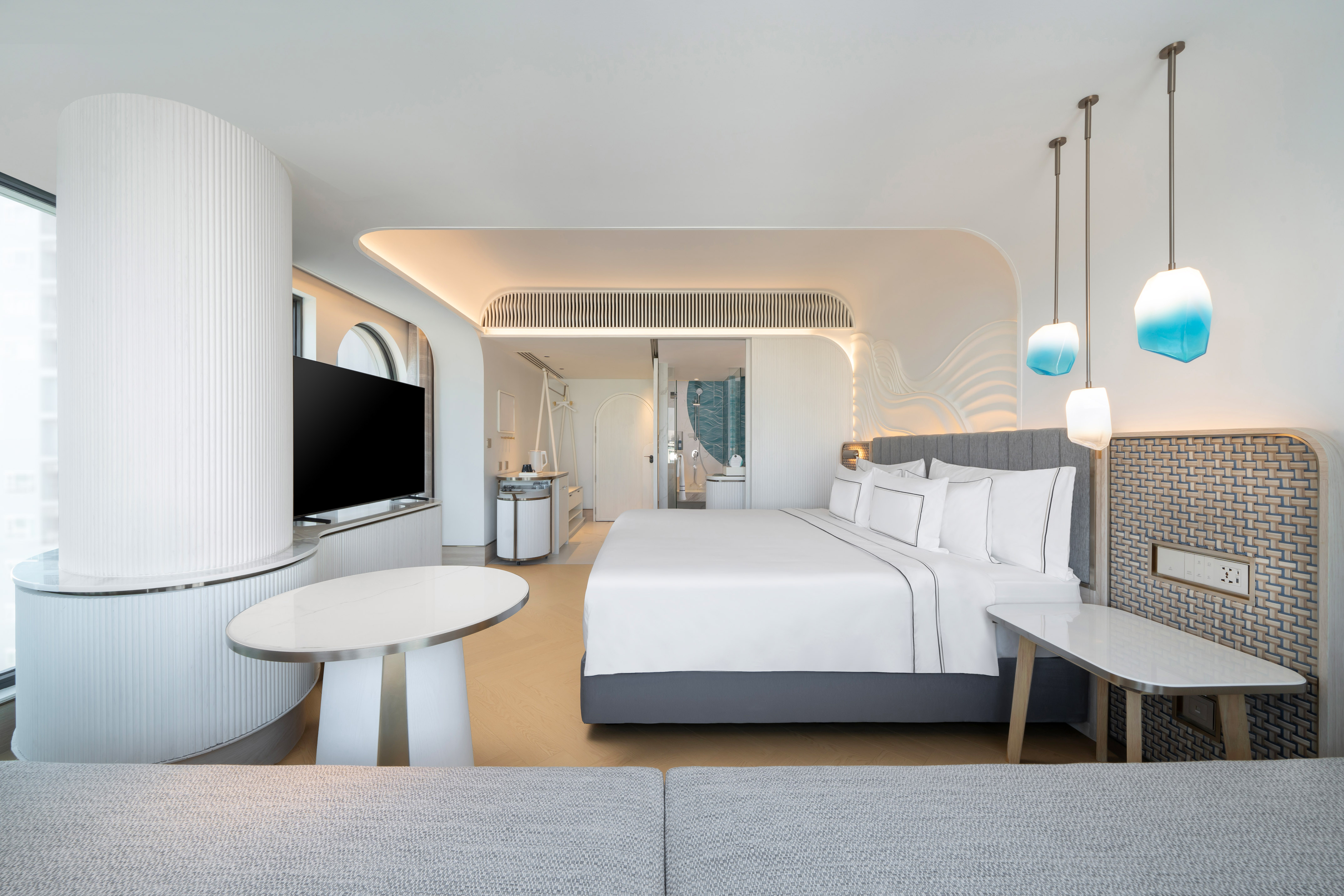 Modern hotel room with king bed, curved walls, and unique blue pendant lamps.