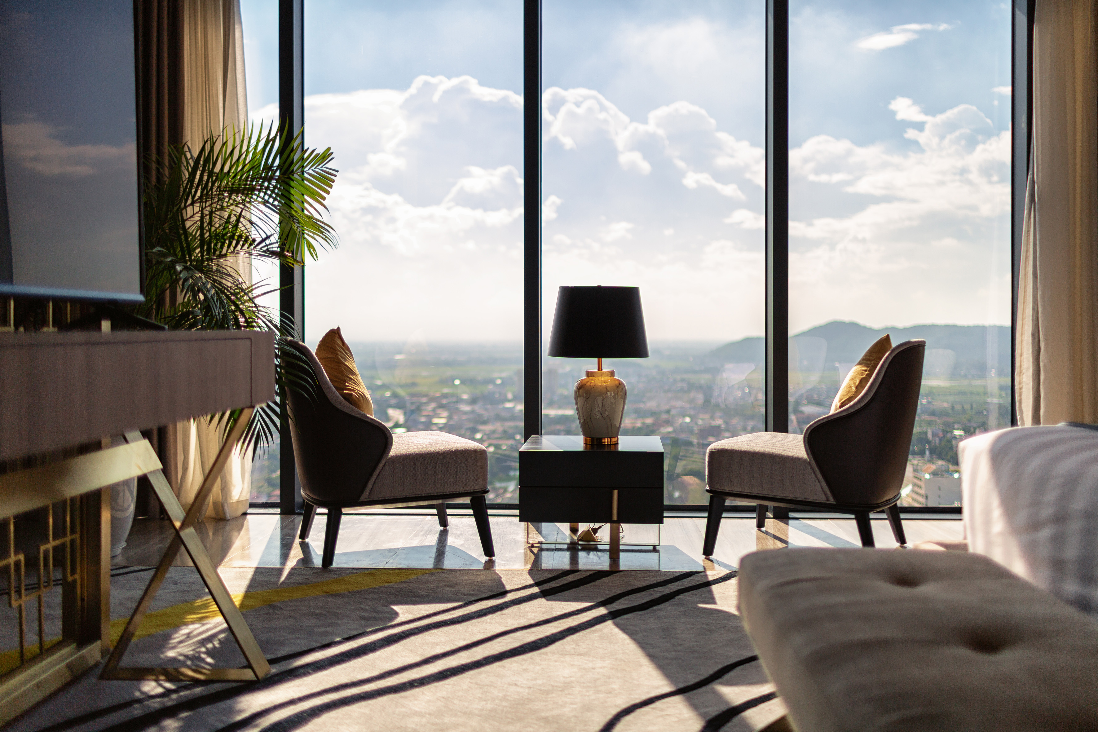 Luxury hotel suite with modern armchairs, side table, and panoramic window city view.