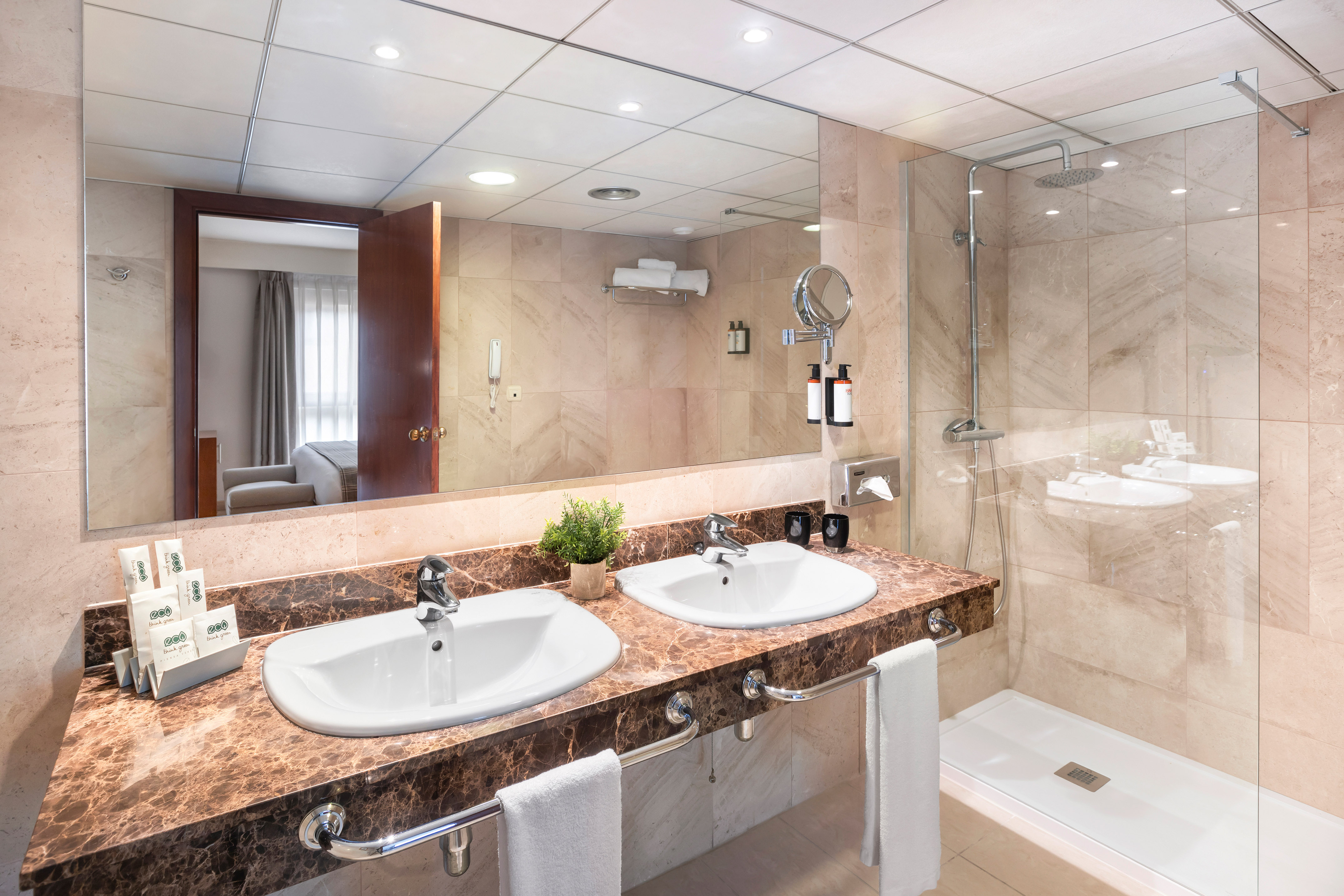 Modern hotel bathroom with double vanity, marble counter, large mirror, and walk-in shower.