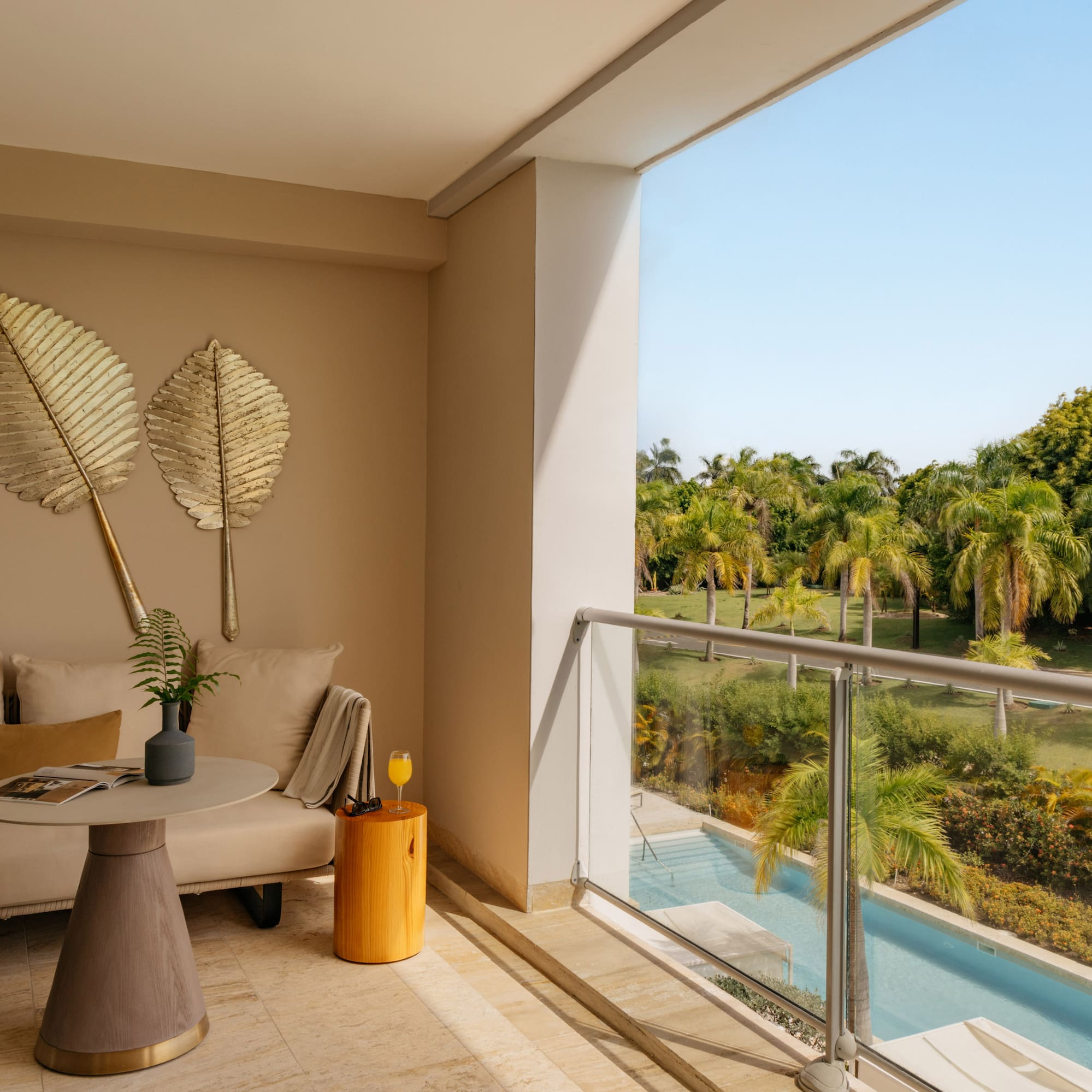 Luxury balcony lounge with golden decor, tropical pool, and palm tree view.