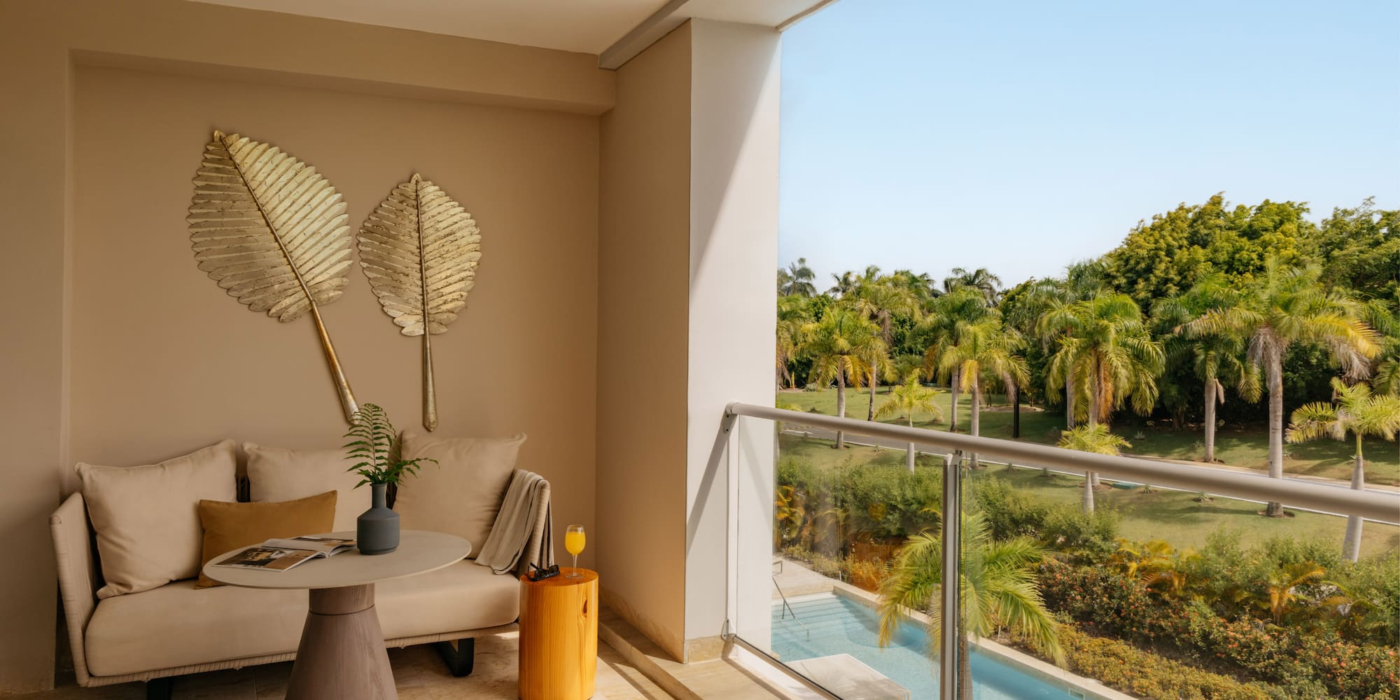 Modern balcony with sofa, tropical palm trees, swimming pool view, and blue sky.