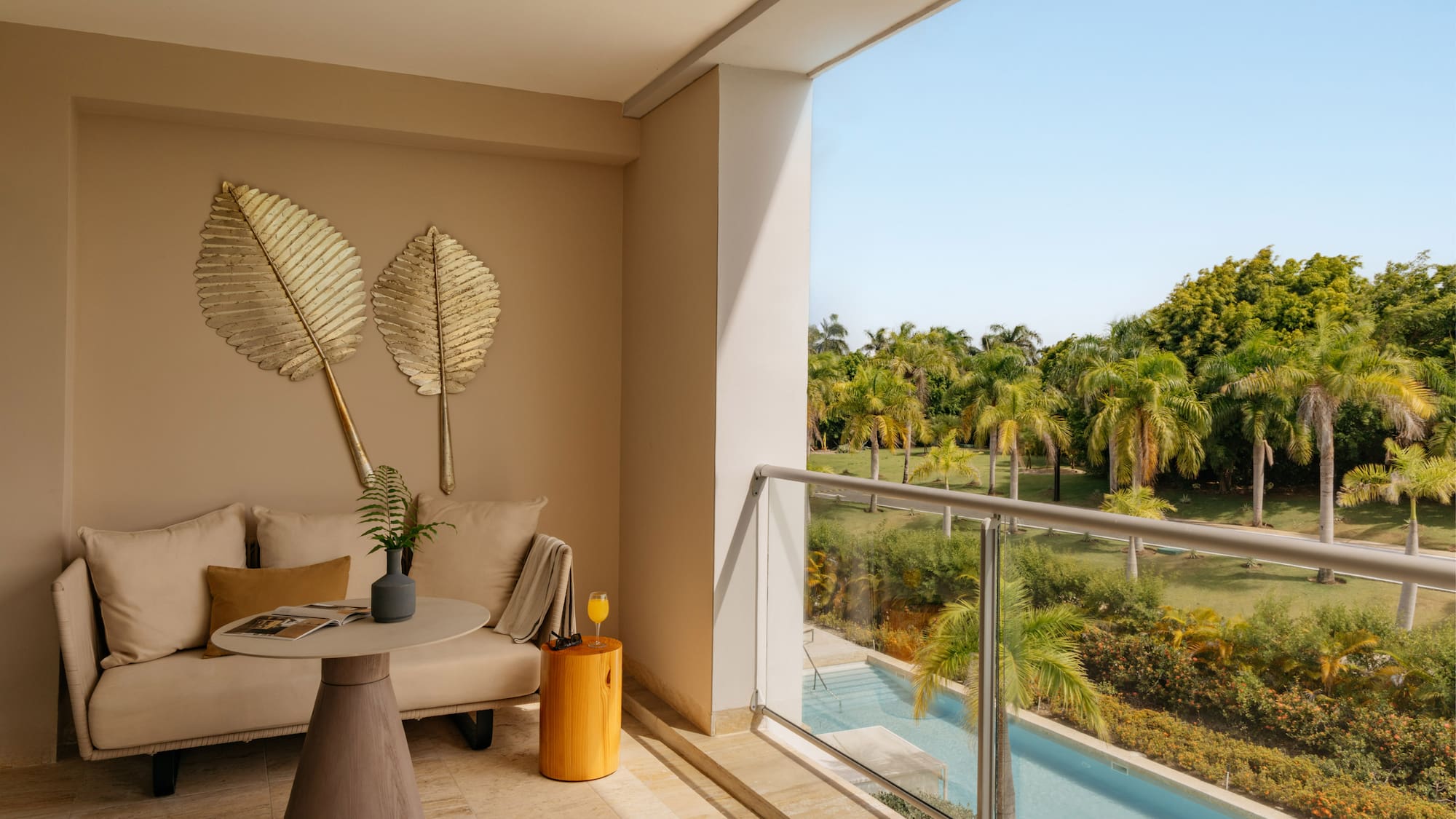 Modern balcony with sofa, tropical palm trees, swimming pool view, and blue sky.