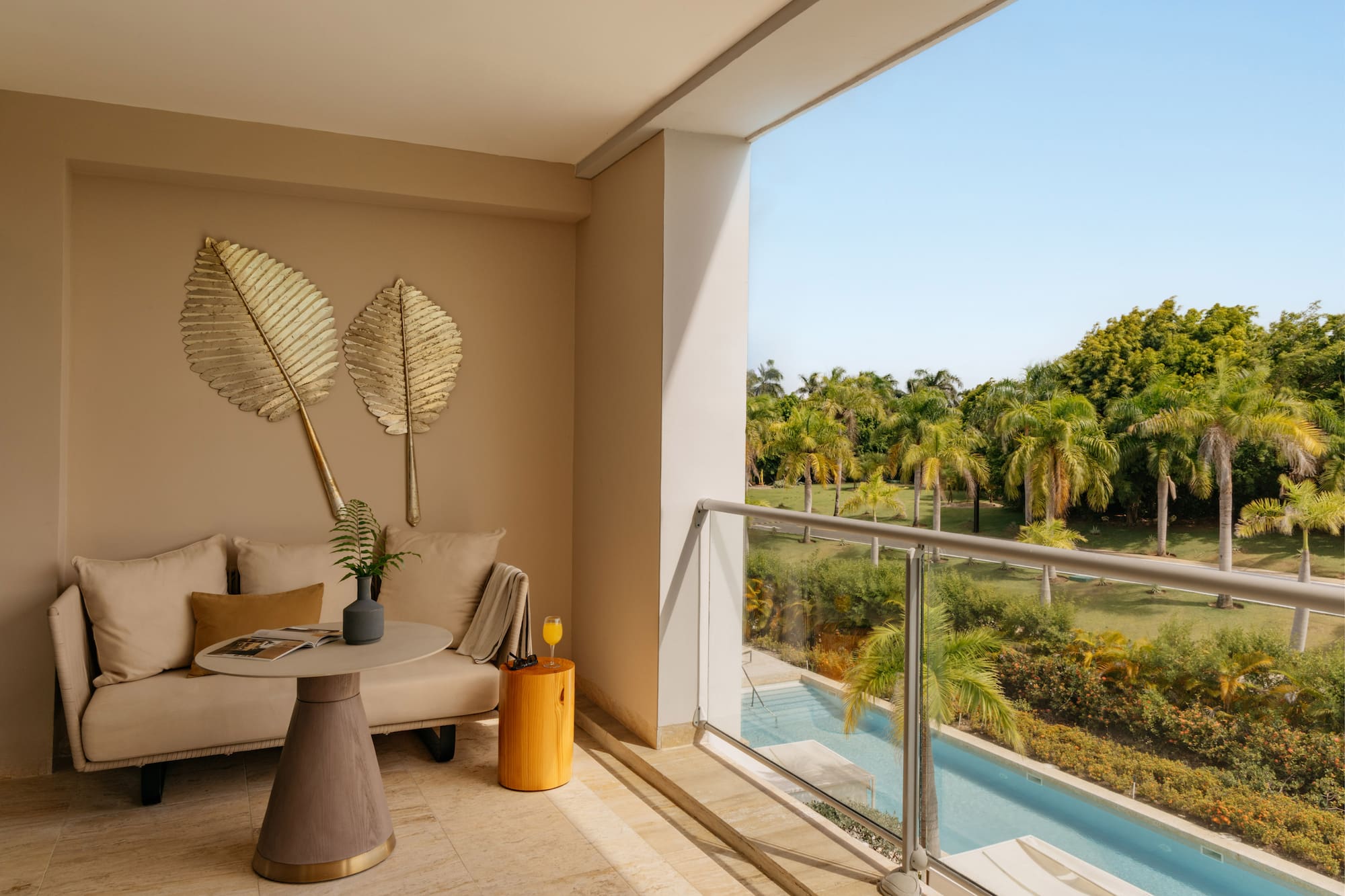 Modern balcony with sofa, tropical palm trees, swimming pool view, and blue sky.