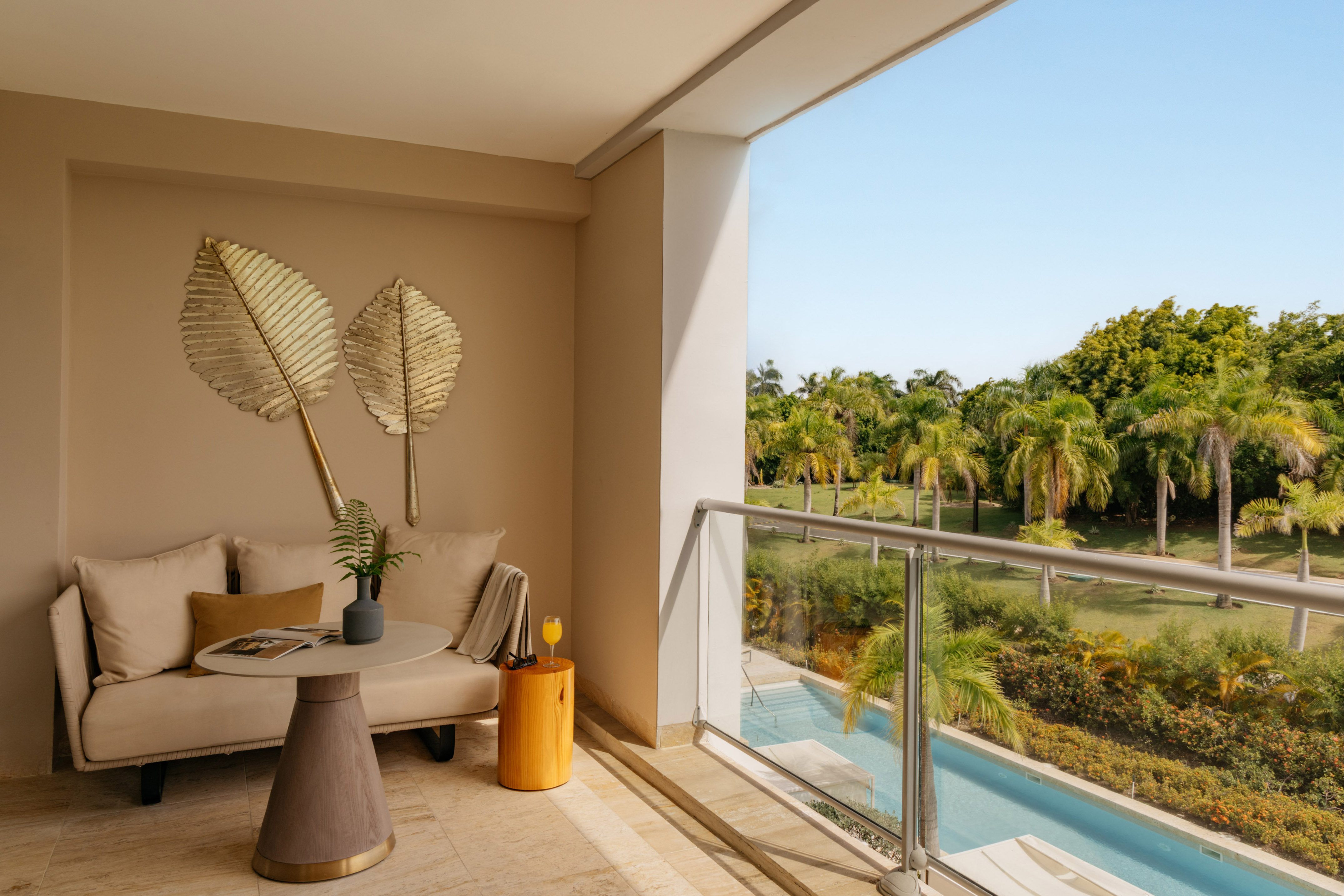 Modern balcony with sofa, tropical palm trees, swimming pool view, and blue sky.
