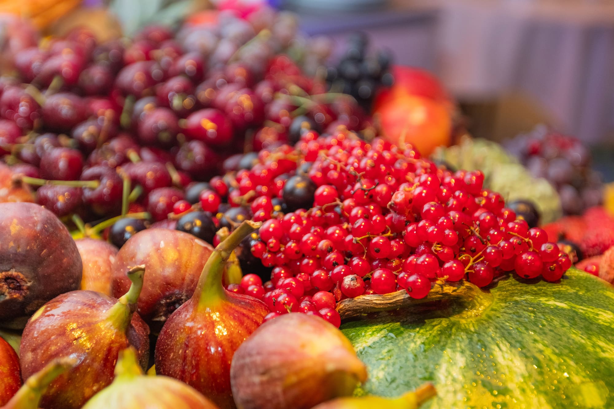 Frutas frescas: grosellas rojas, higos, uvas y sandía en exhibición.