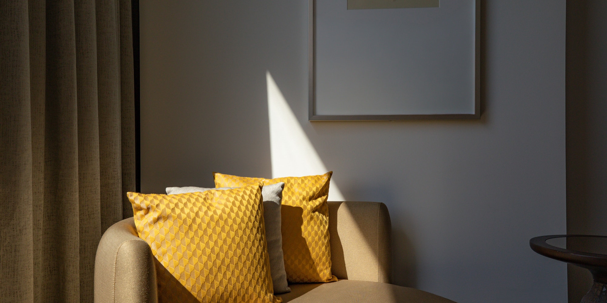 Sunlit chaise lounge with yellow geometric pillows, framed art, and drapes.