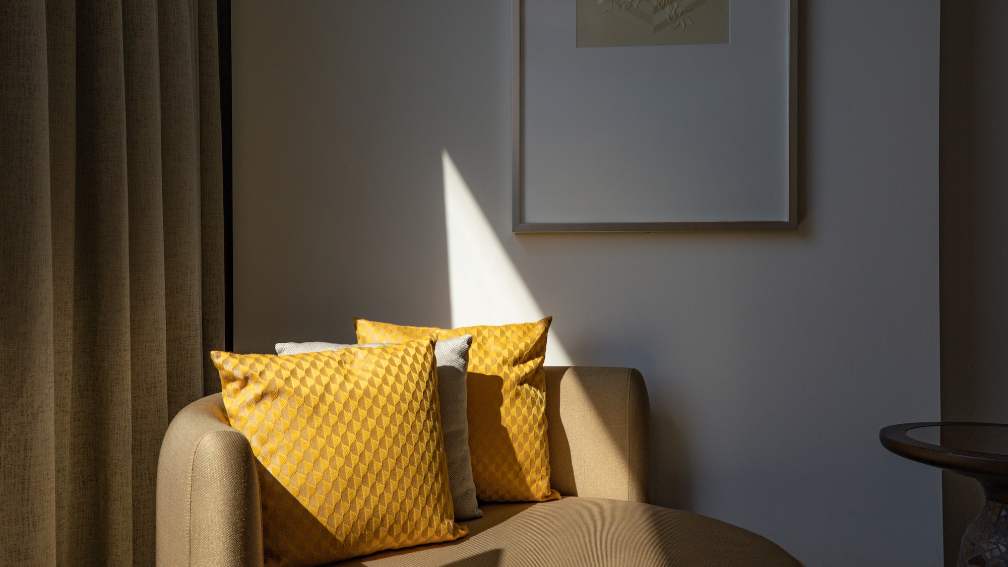 Sunlit chaise lounge with yellow geometric pillows, framed art, and drapes.