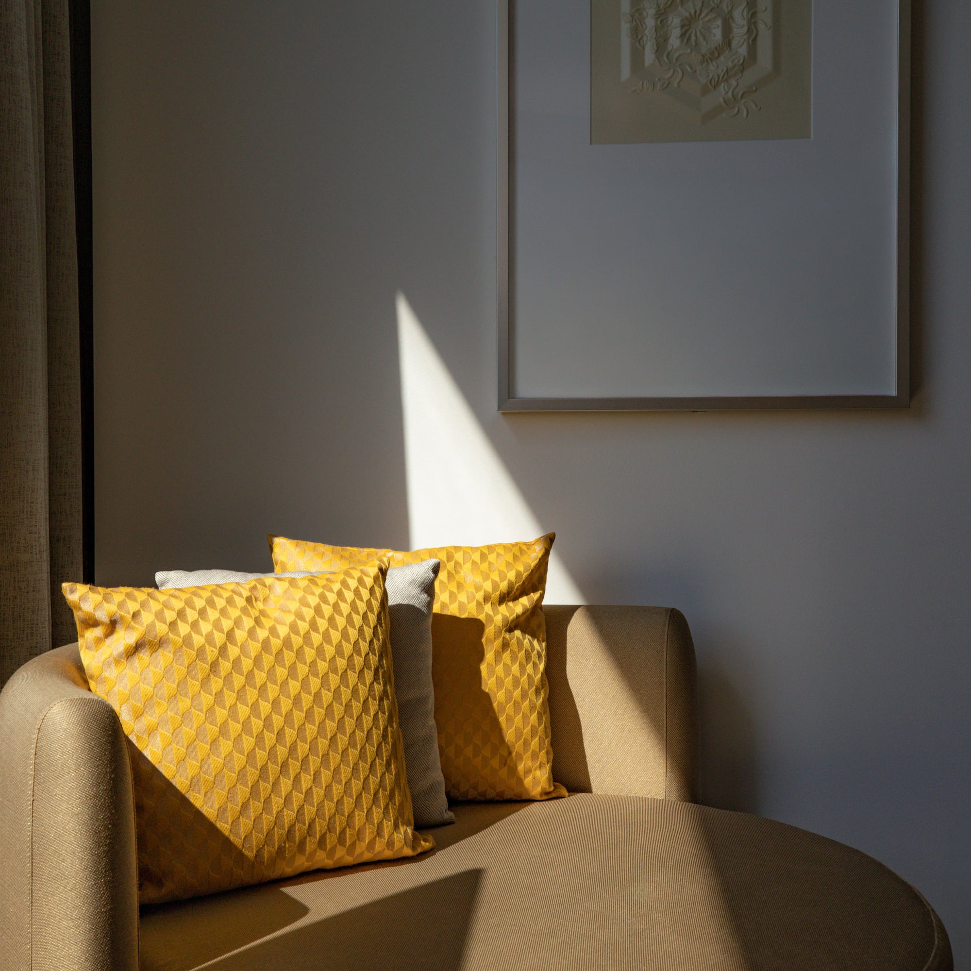 Sunlit chaise lounge with yellow geometric pillows, framed art, and drapes.