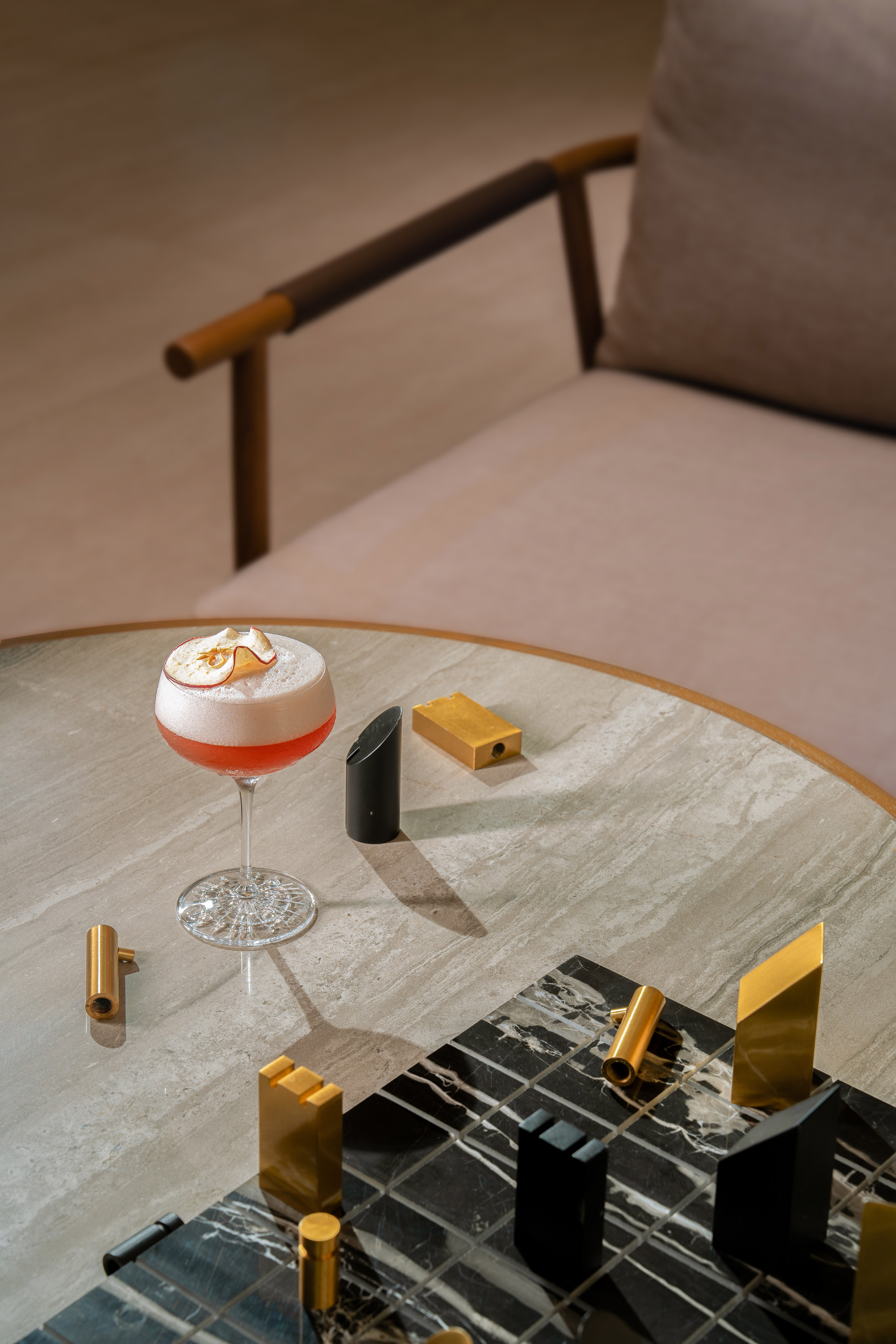 Foamy pink cocktail with apple garnish on a marble table with modern chess set.