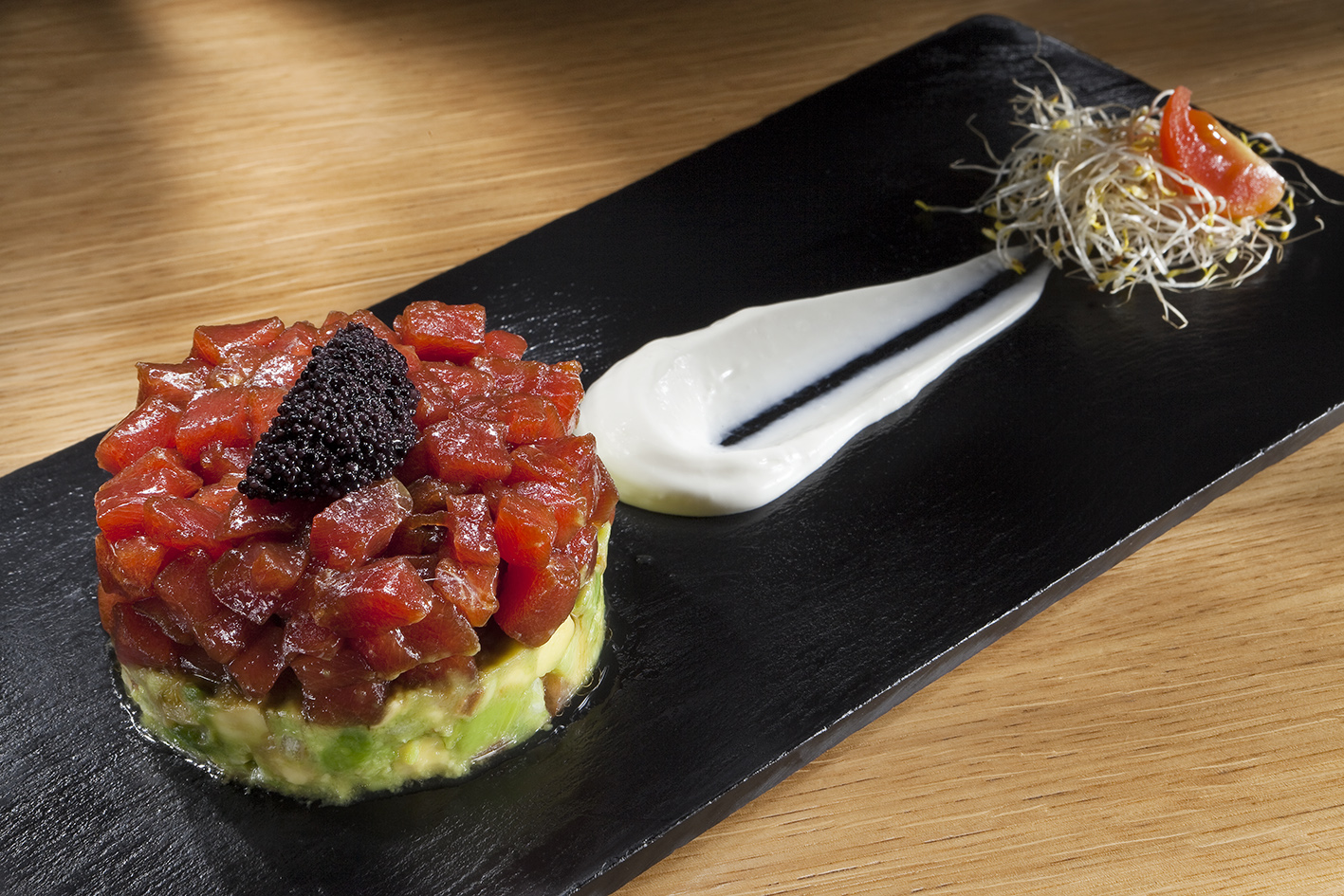 Tuna and avocado tartare topped with caviar on black slate plate.