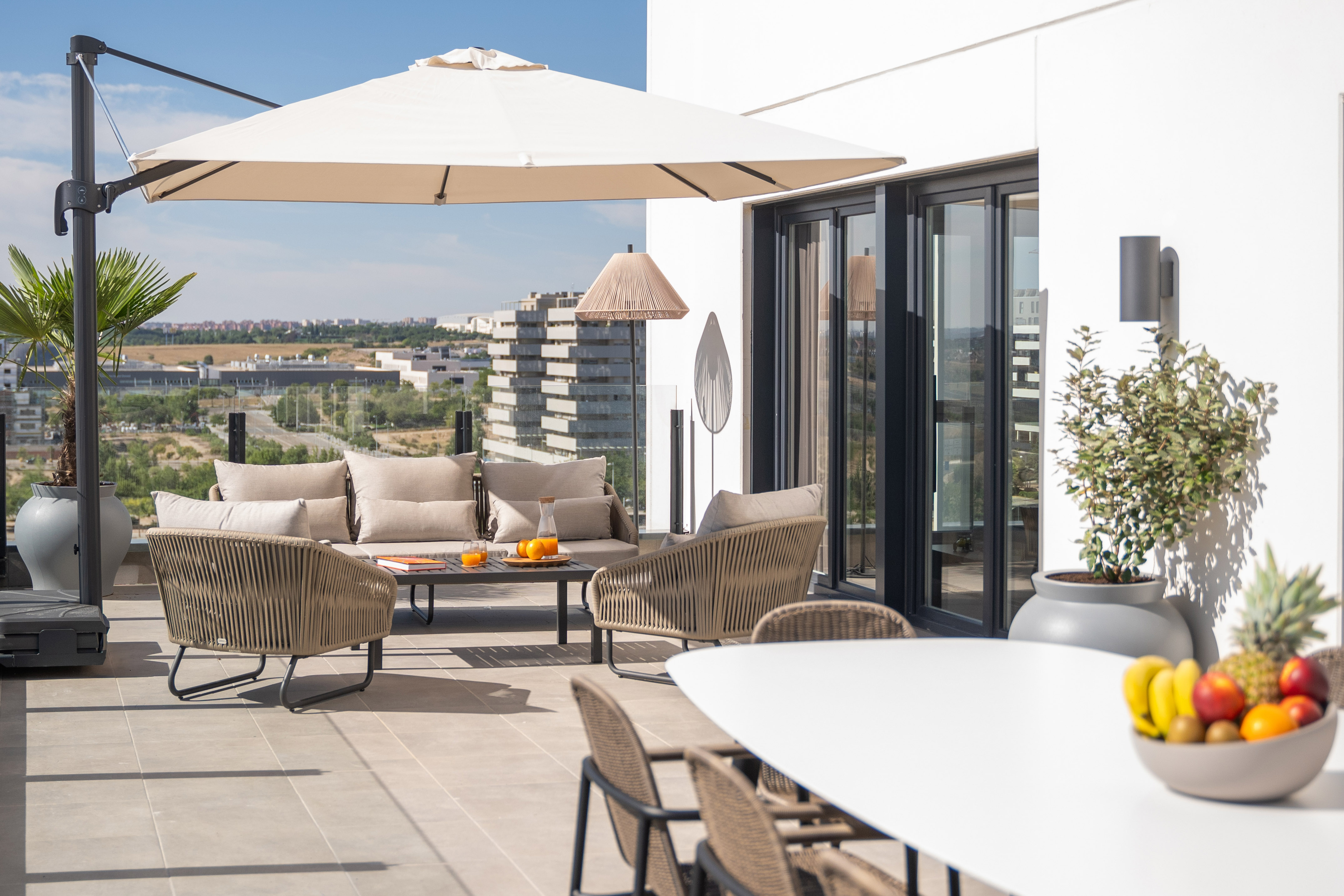 Modern outdoor lounge furniture on a bright patio with a city view and umbrella.