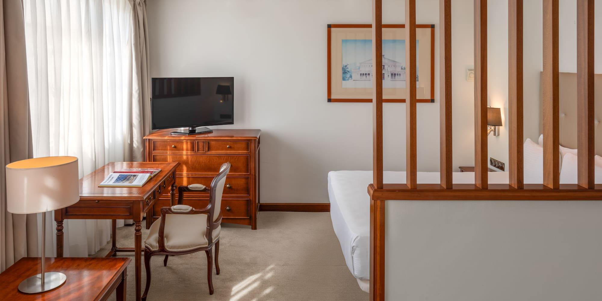 Cozy hotel studio room with desk, TV, and bed separated by wooden partition.