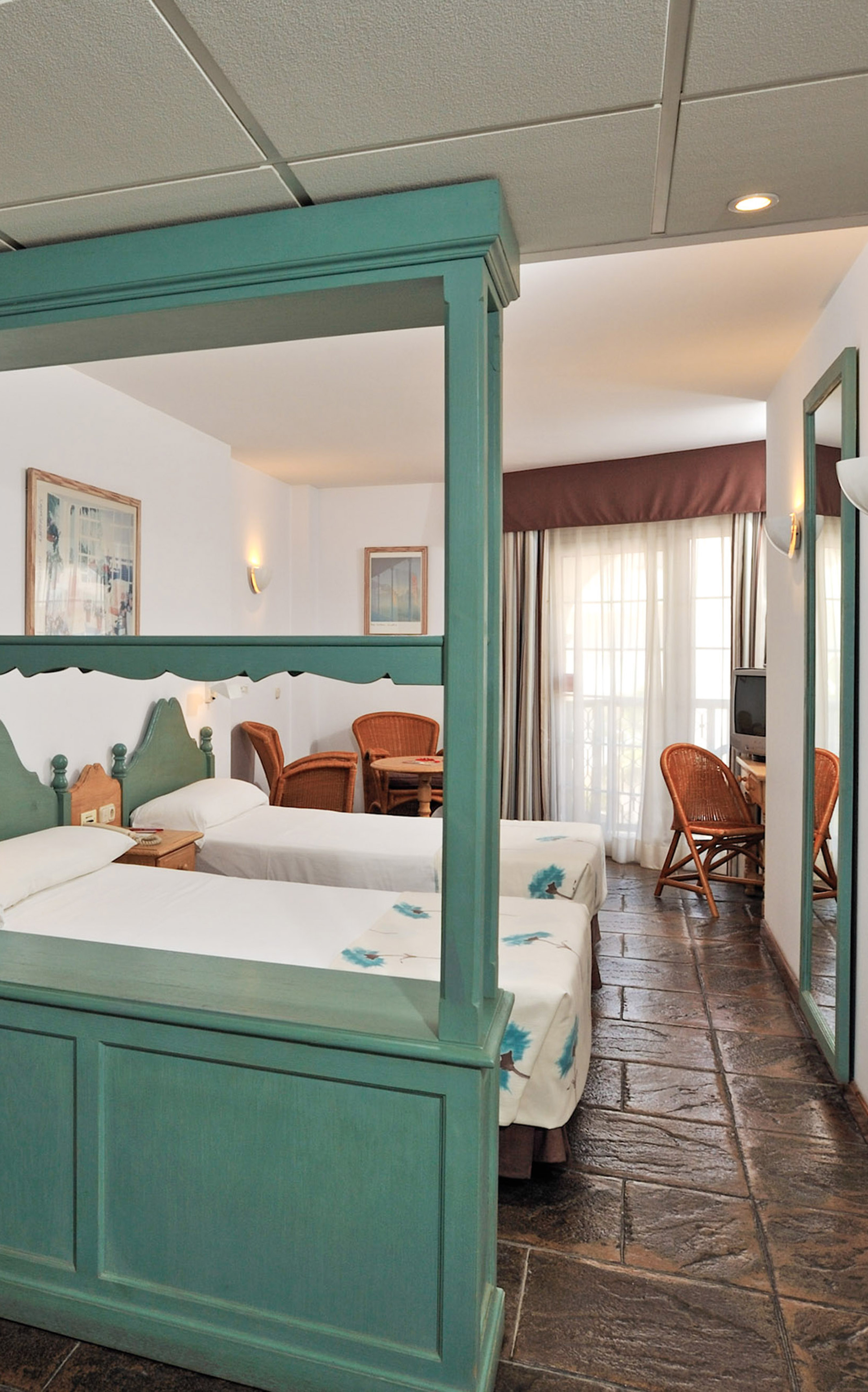 Resort twin bedroom with teal beds, stone floor, and bright balcony.