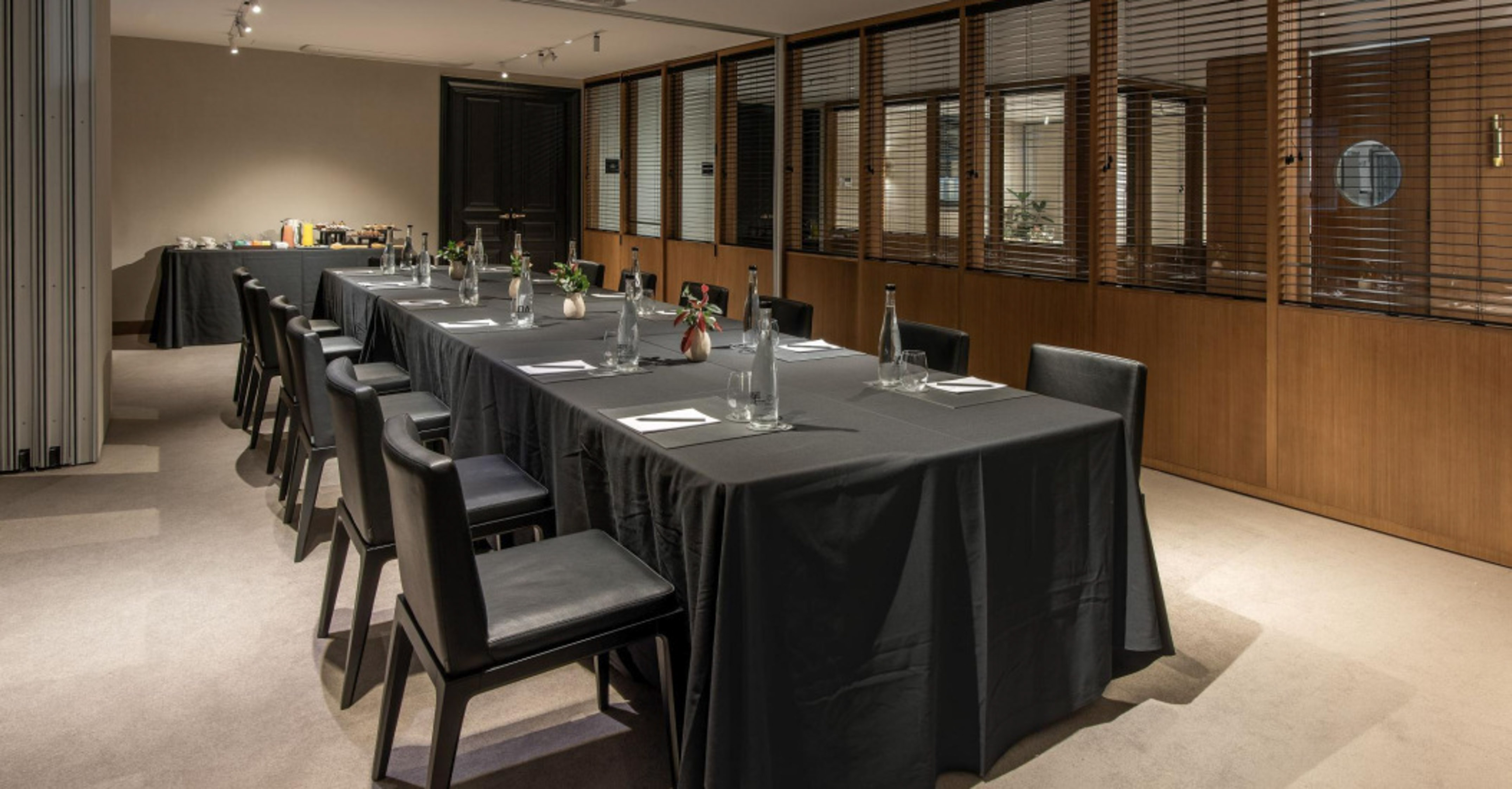 Elegant private meeting room with long black table, chairs, and refreshments.