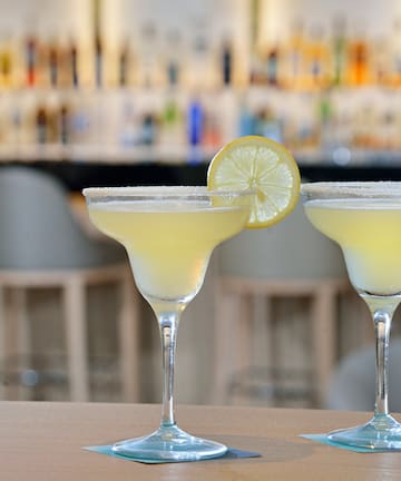 two glasses of yellow liquid with lemon slices on top of them