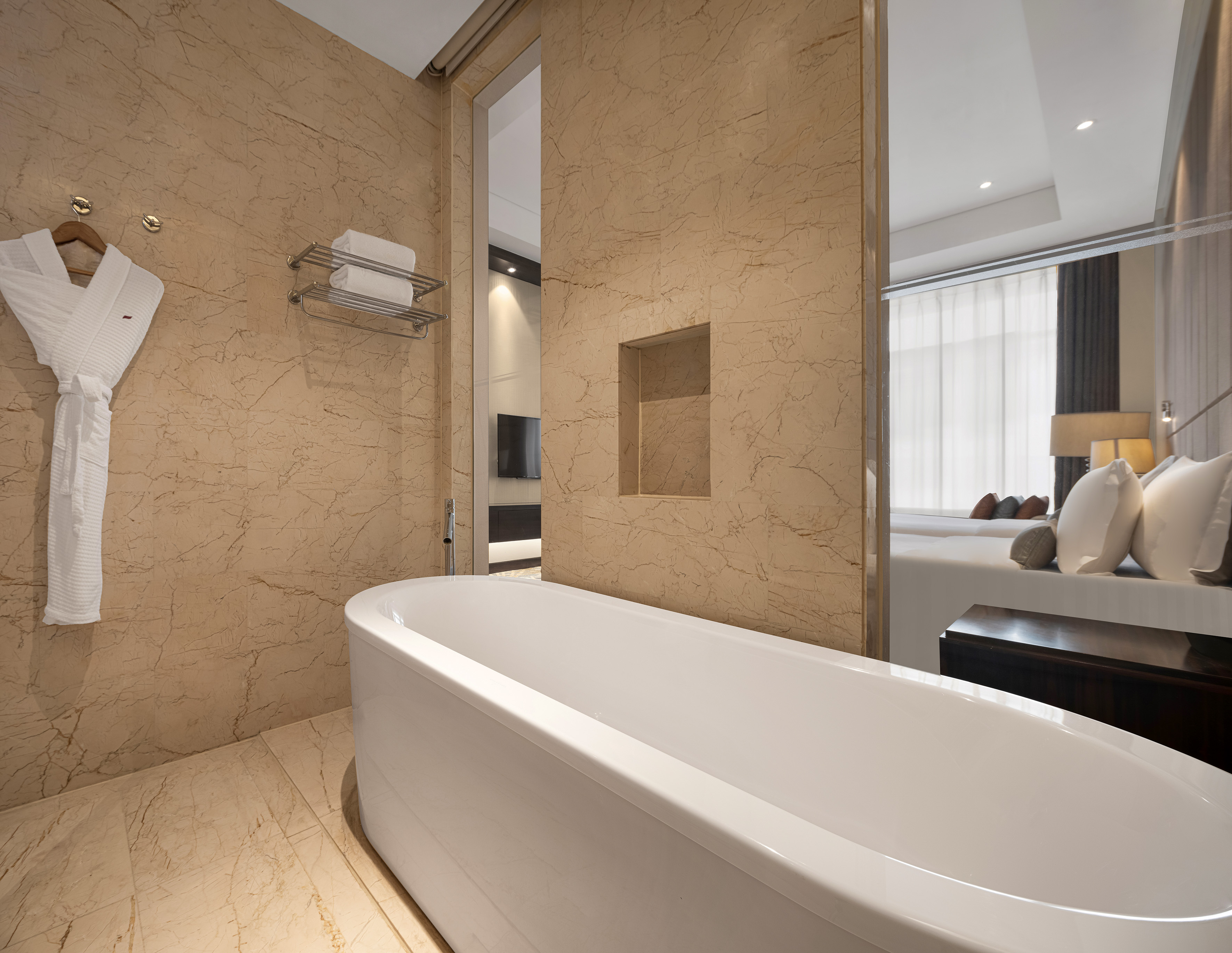 Modern hotel bathroom with freestanding bathtub, marble walls, and bedroom view.