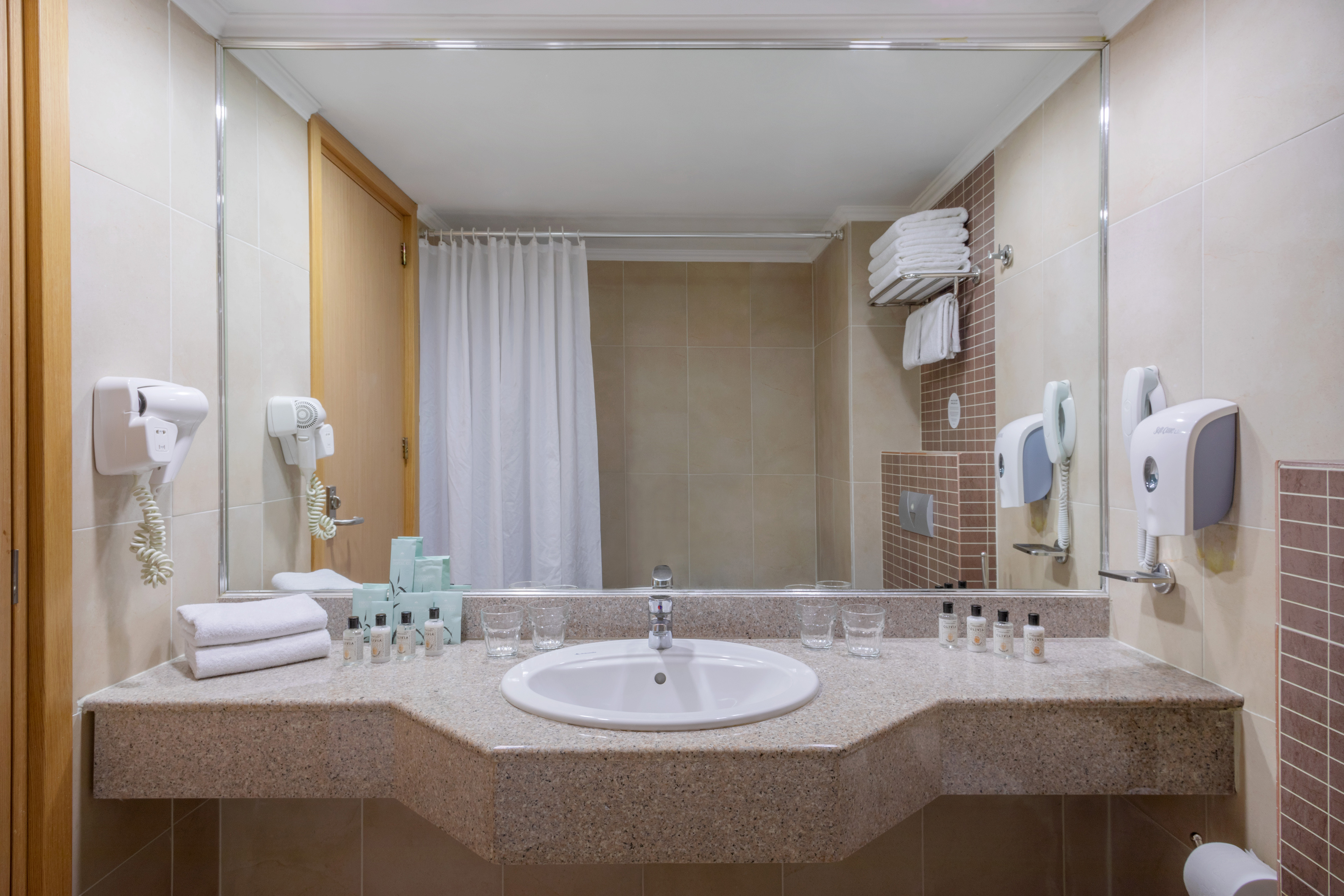 Hotel bathroom vanity with sink, mirror, toiletries, and hairdryer.