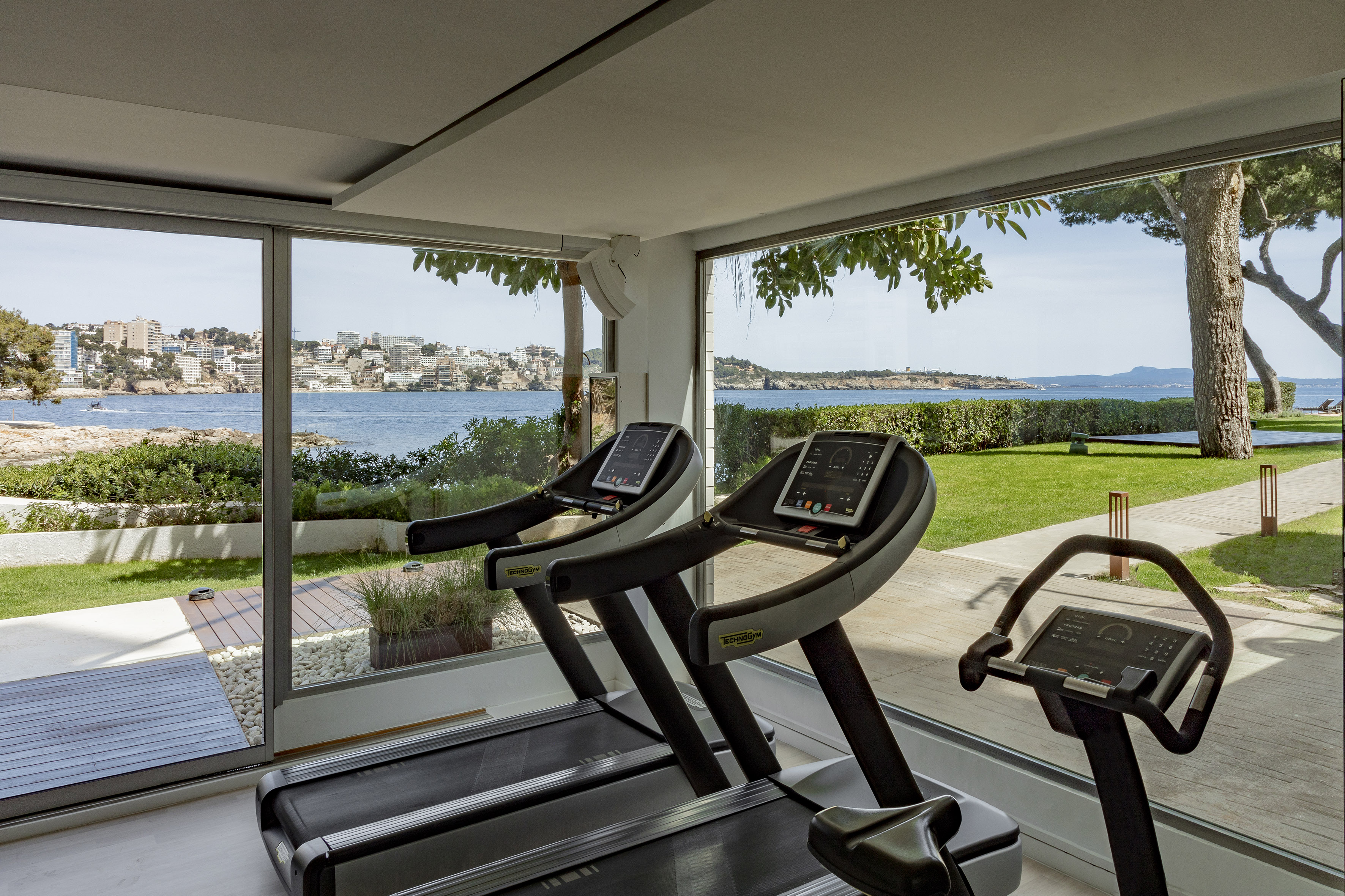 Technogym treadmills in gym with panoramic ocean and coastal town view.