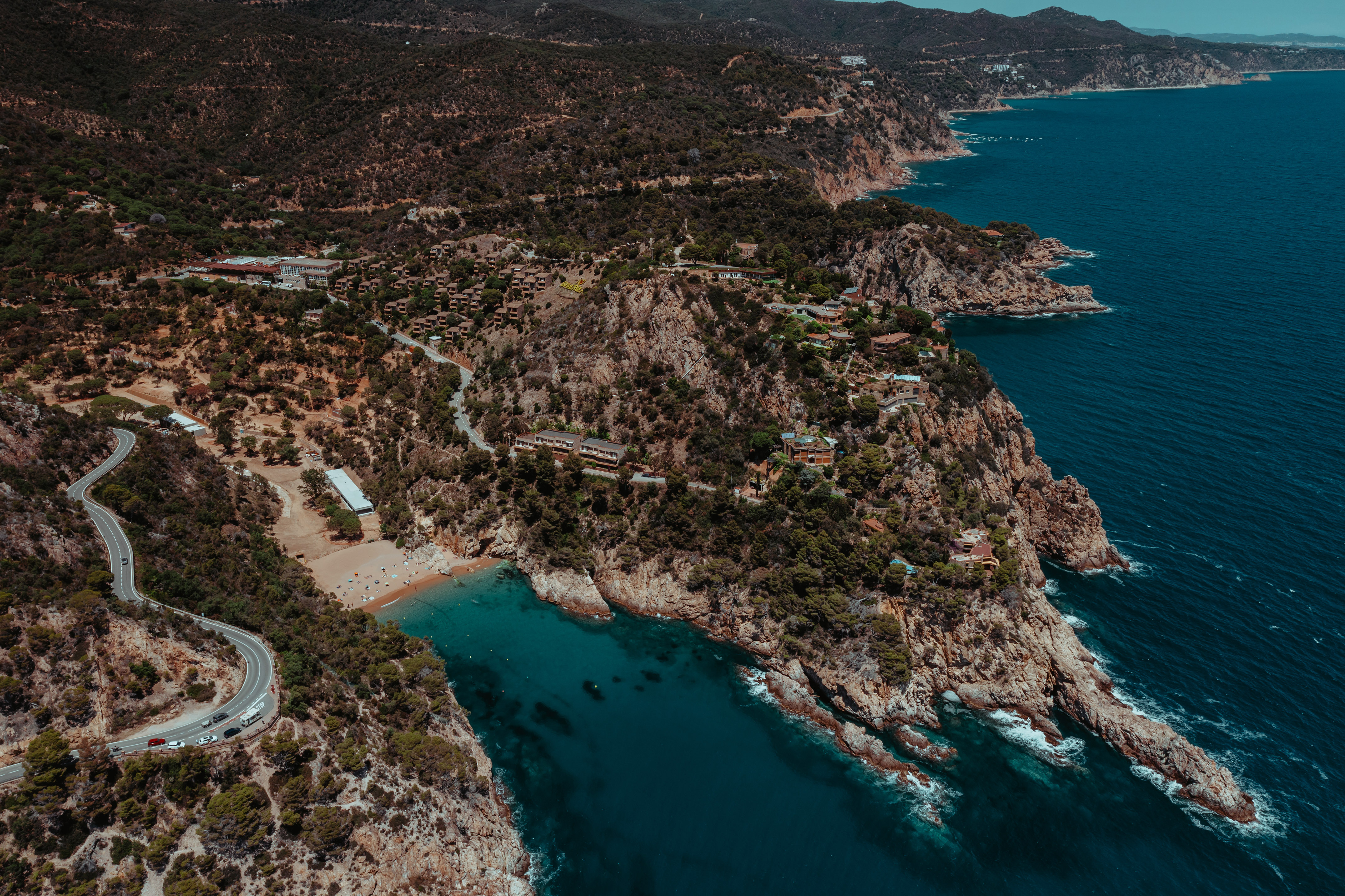 Winding coastal road, cliffside village, beach coves, rocky Mediterranean shore.