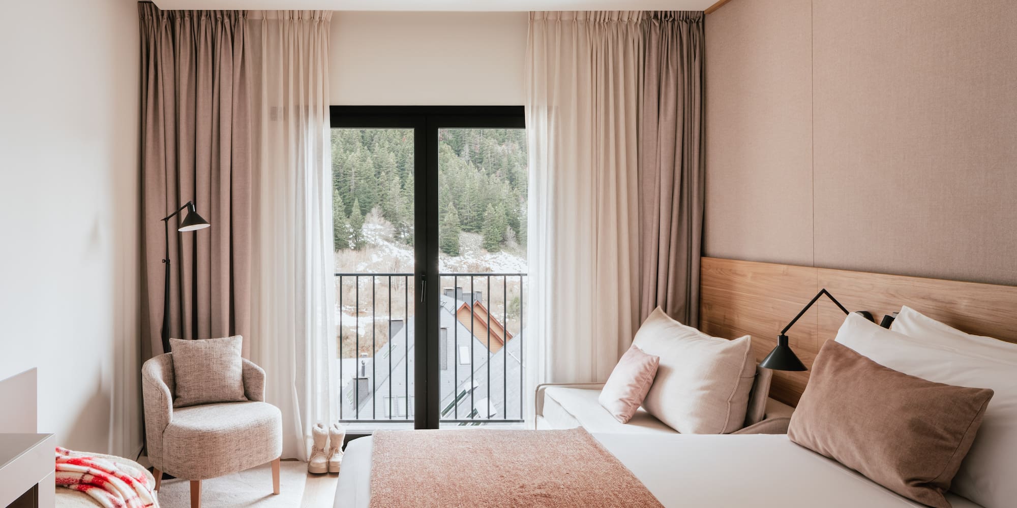 Modern hotel bedroom with mountain view balcony, cozy armchair, and neutral decor.