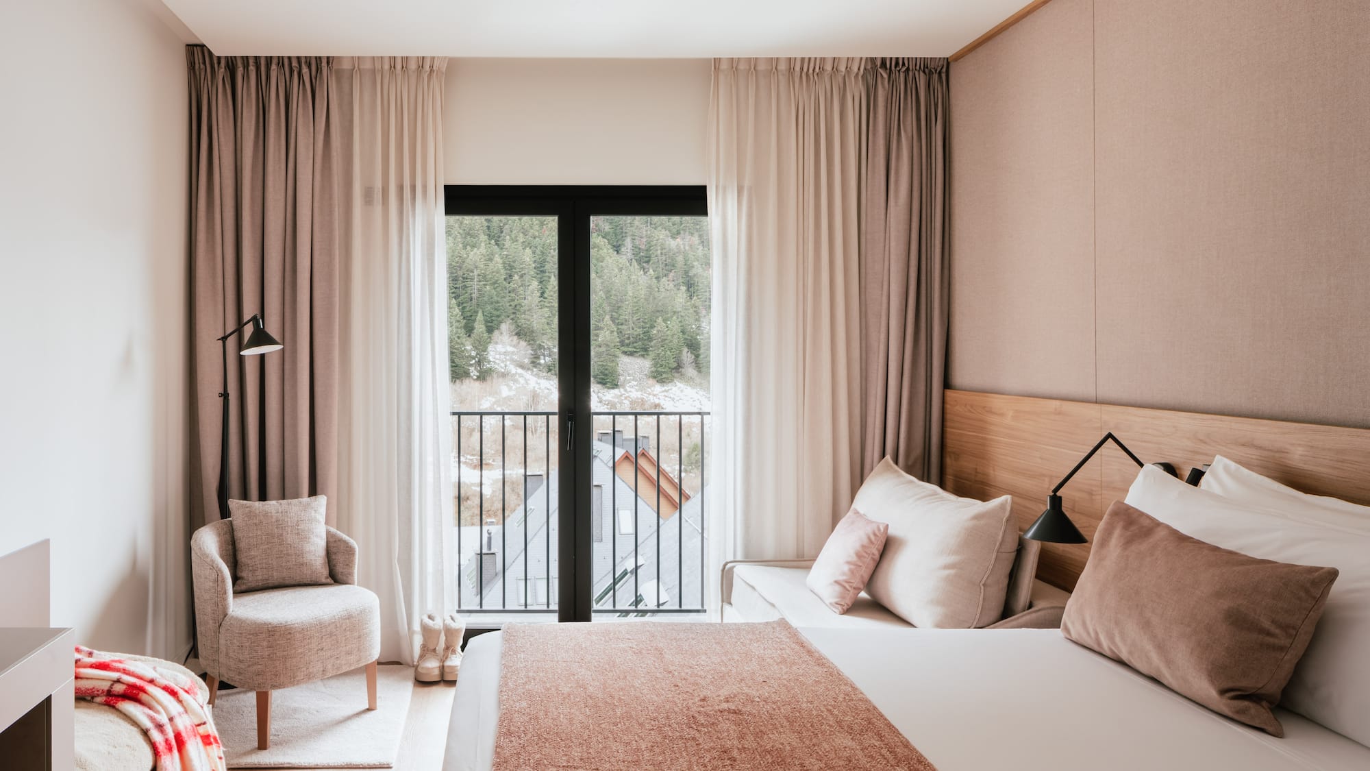 Modern hotel bedroom with mountain view balcony, cozy armchair, and neutral decor.
