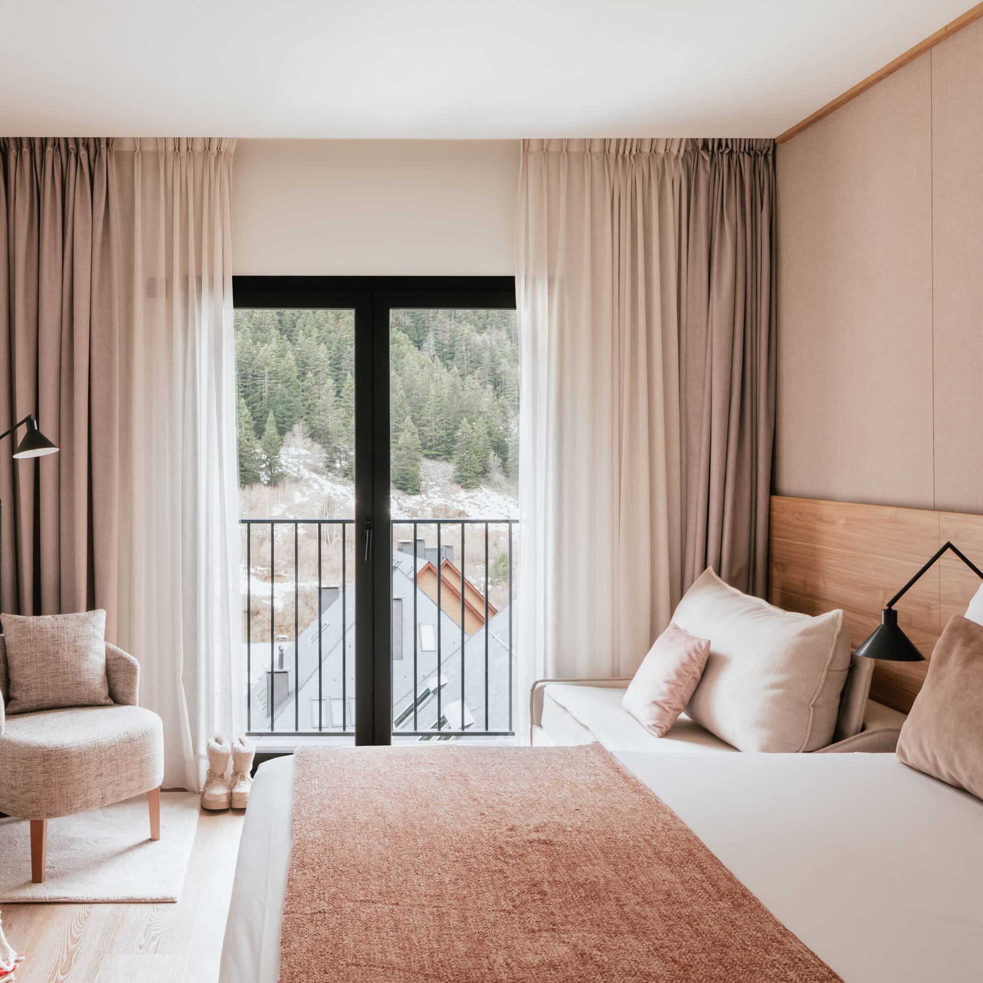 Modern hotel bedroom with mountain view balcony, cozy armchair, and neutral decor.