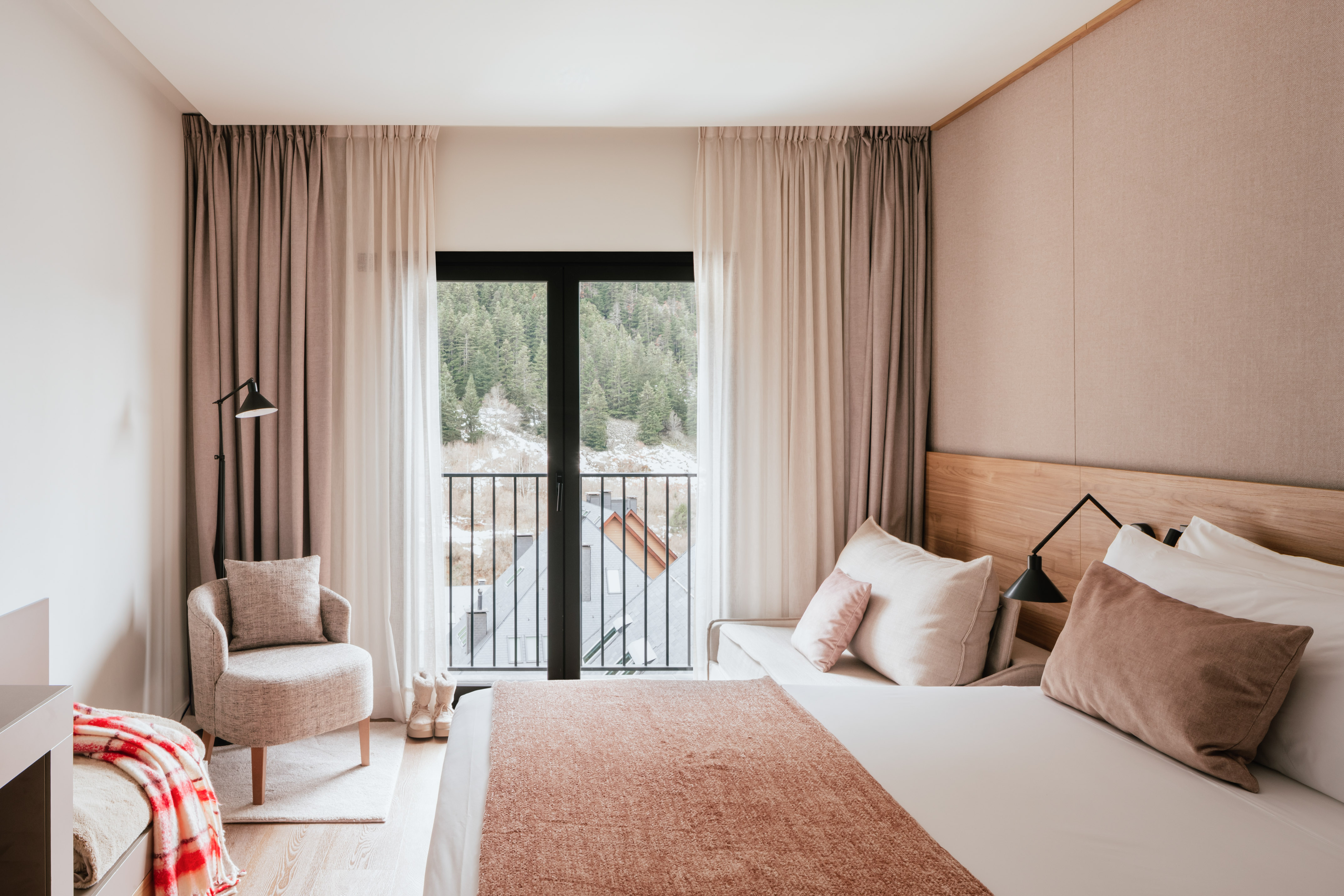 Modern hotel bedroom with mountain view balcony, cozy armchair, and neutral decor.