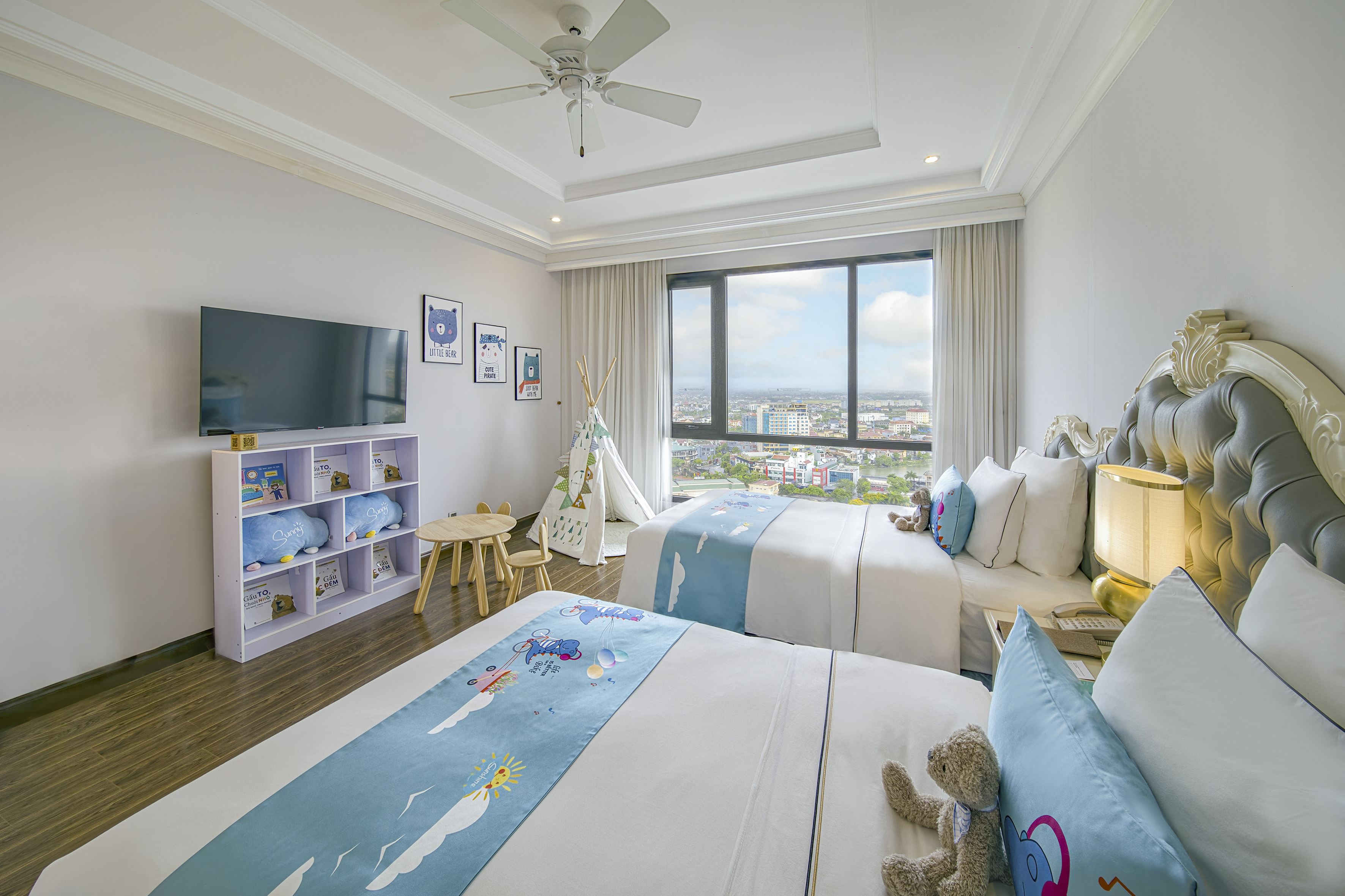 Kids' hotel room with twin beds, city view, teepee, TV, and playful decor.