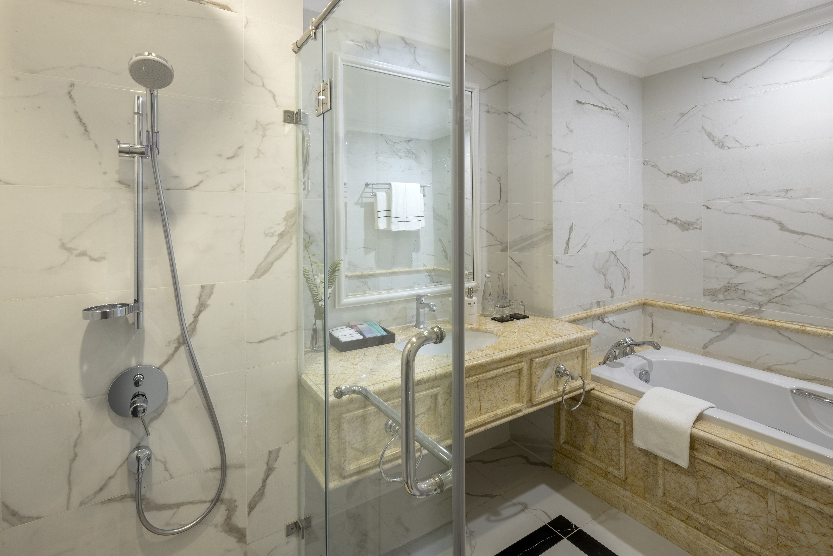 Luxury hotel bathroom with white marble, glass shower, and bathtub.