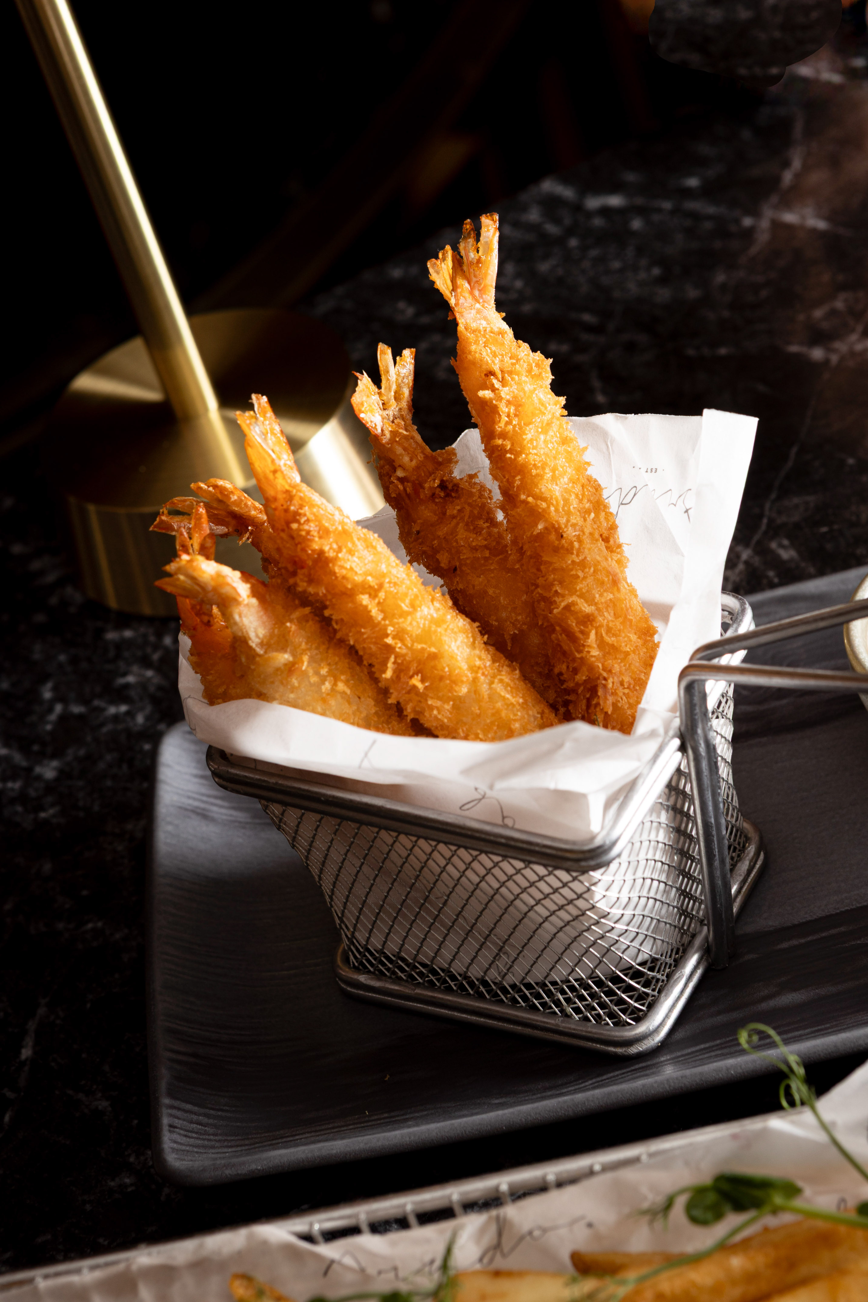 Golden breaded fried shrimp with tails in a metal basket.