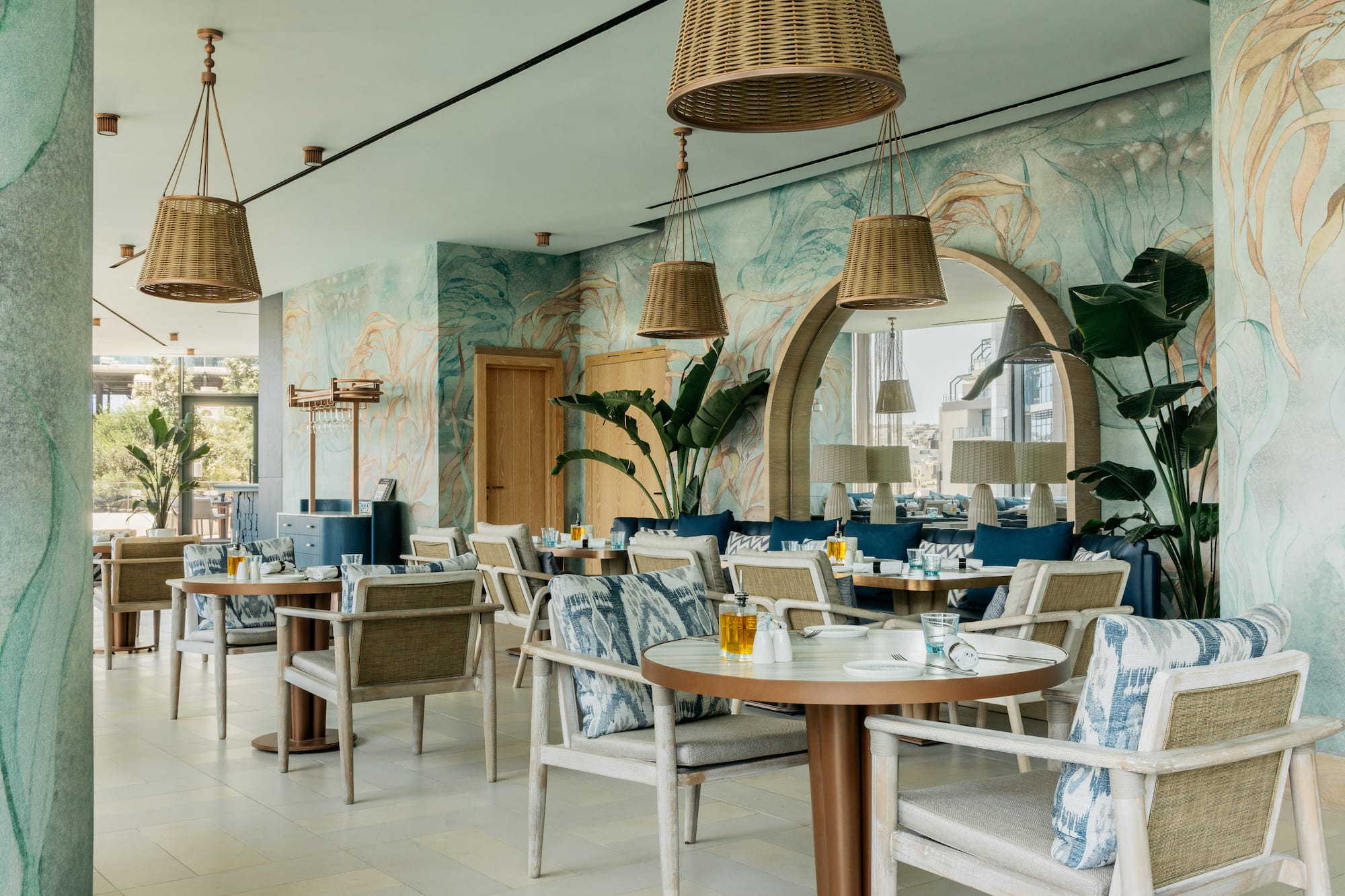 Coastal resort dining room with wicker lighting, patterned chairs, and tropical mural.