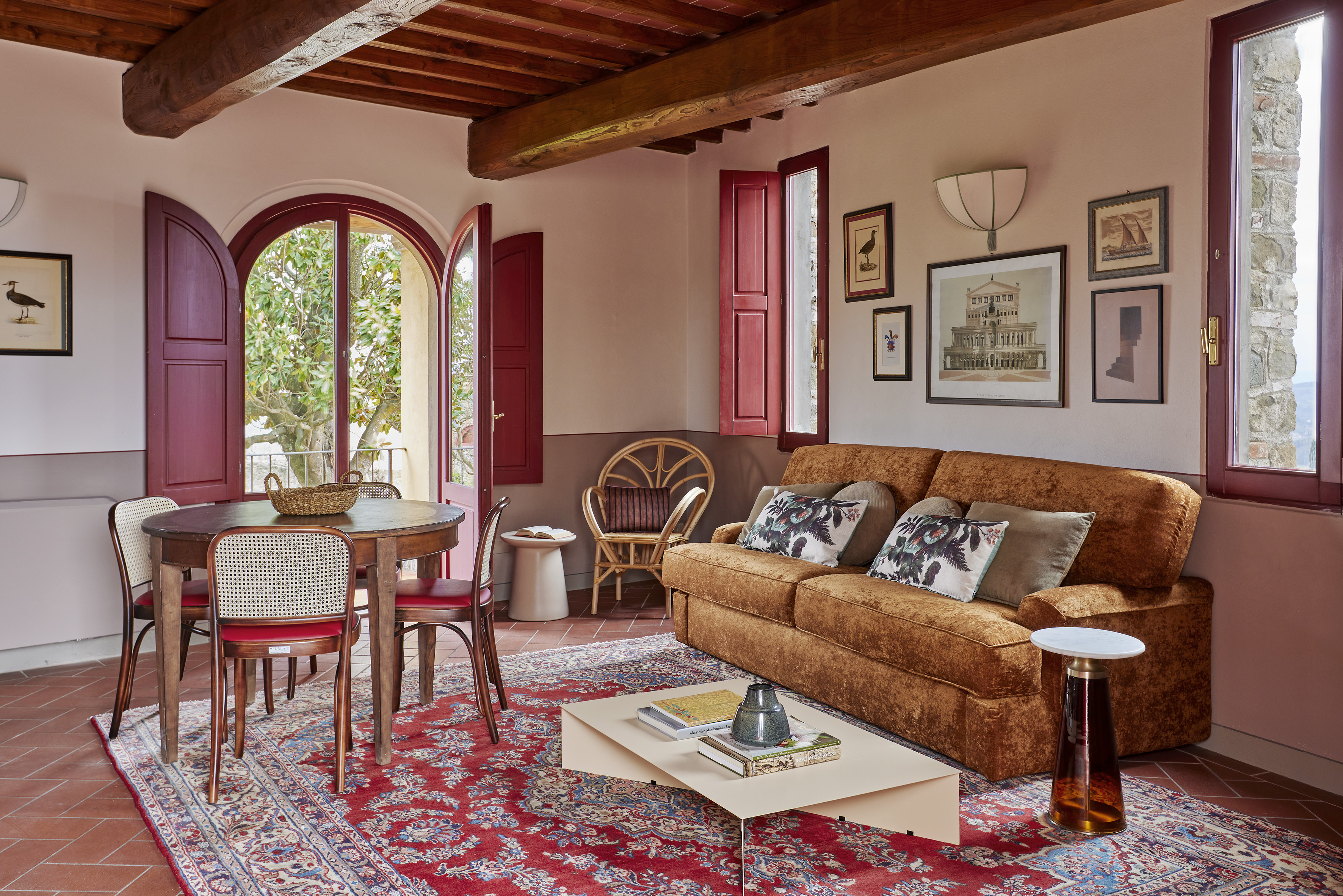 Tuscan living room: red shutters, beamed ceiling, terracotta floor, oriental rug.