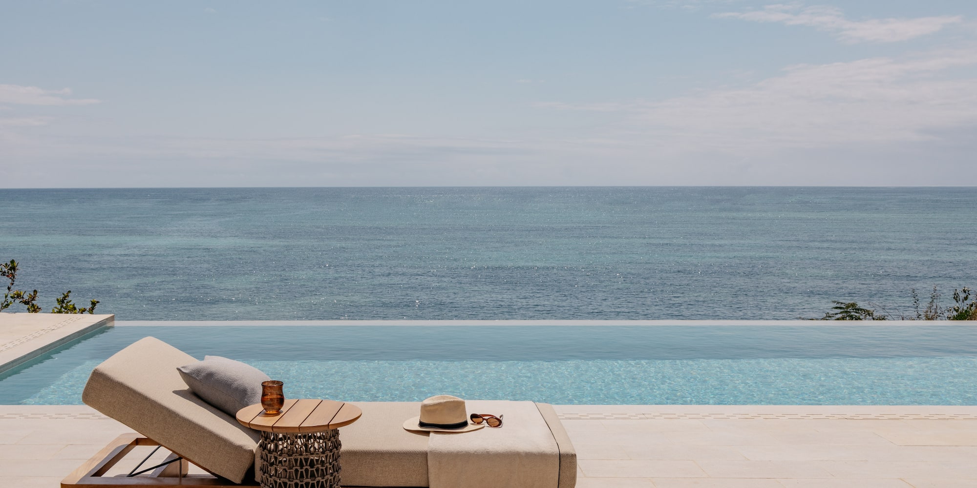 a lounge chair with a hat and sunglasses on it by a pool