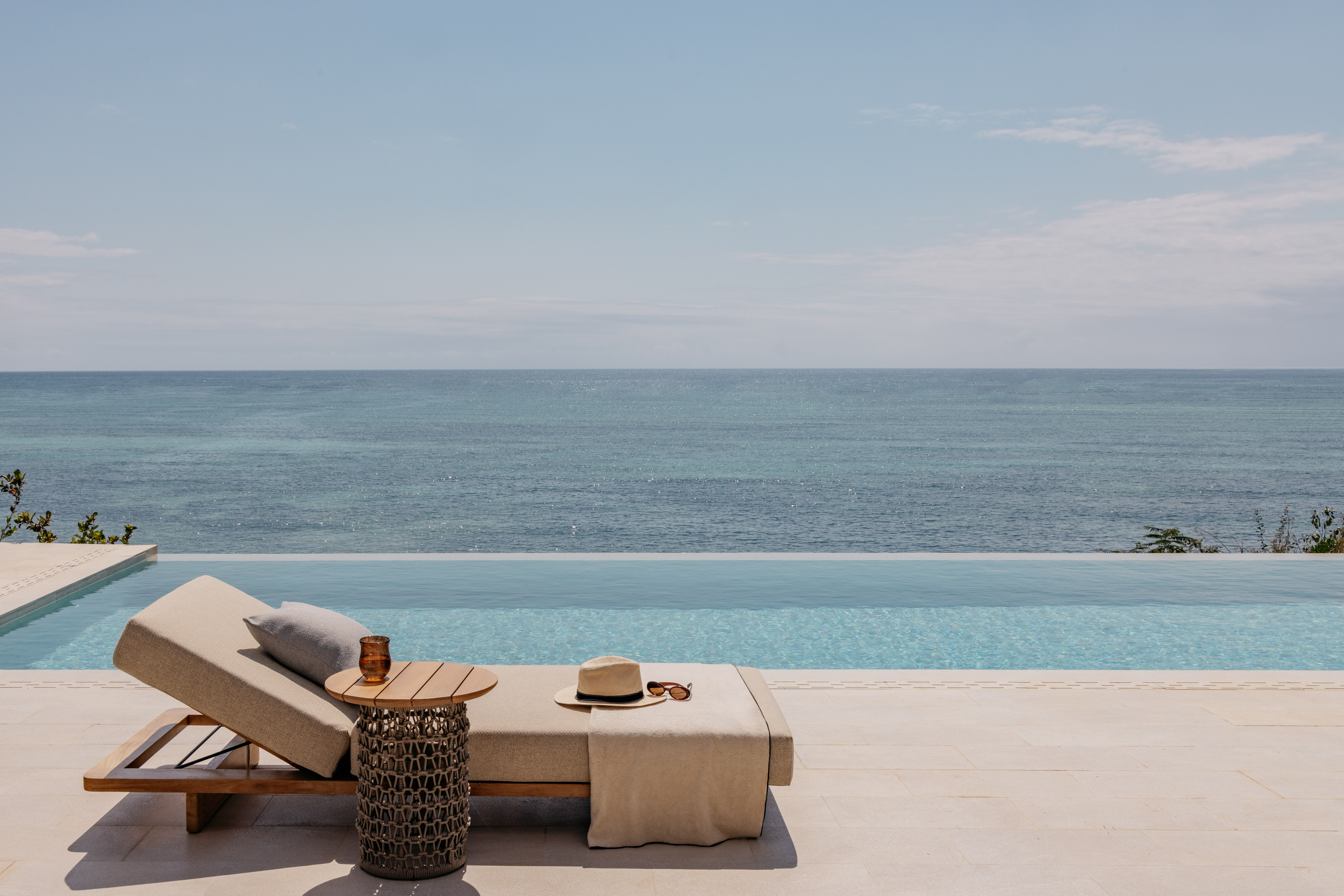 Ocean view infinity pool with a sun lounger, hat, and sunglasses.