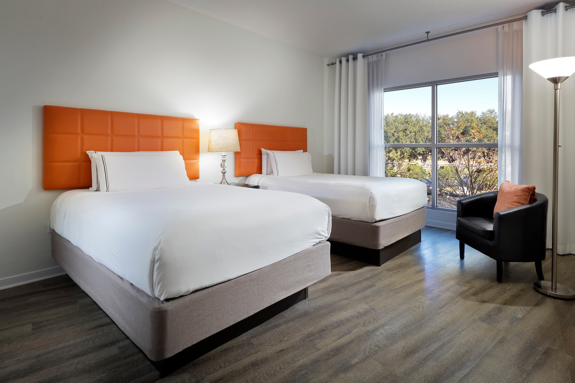 Hotel guest room with two double beds, orange headboards, window, armchair.