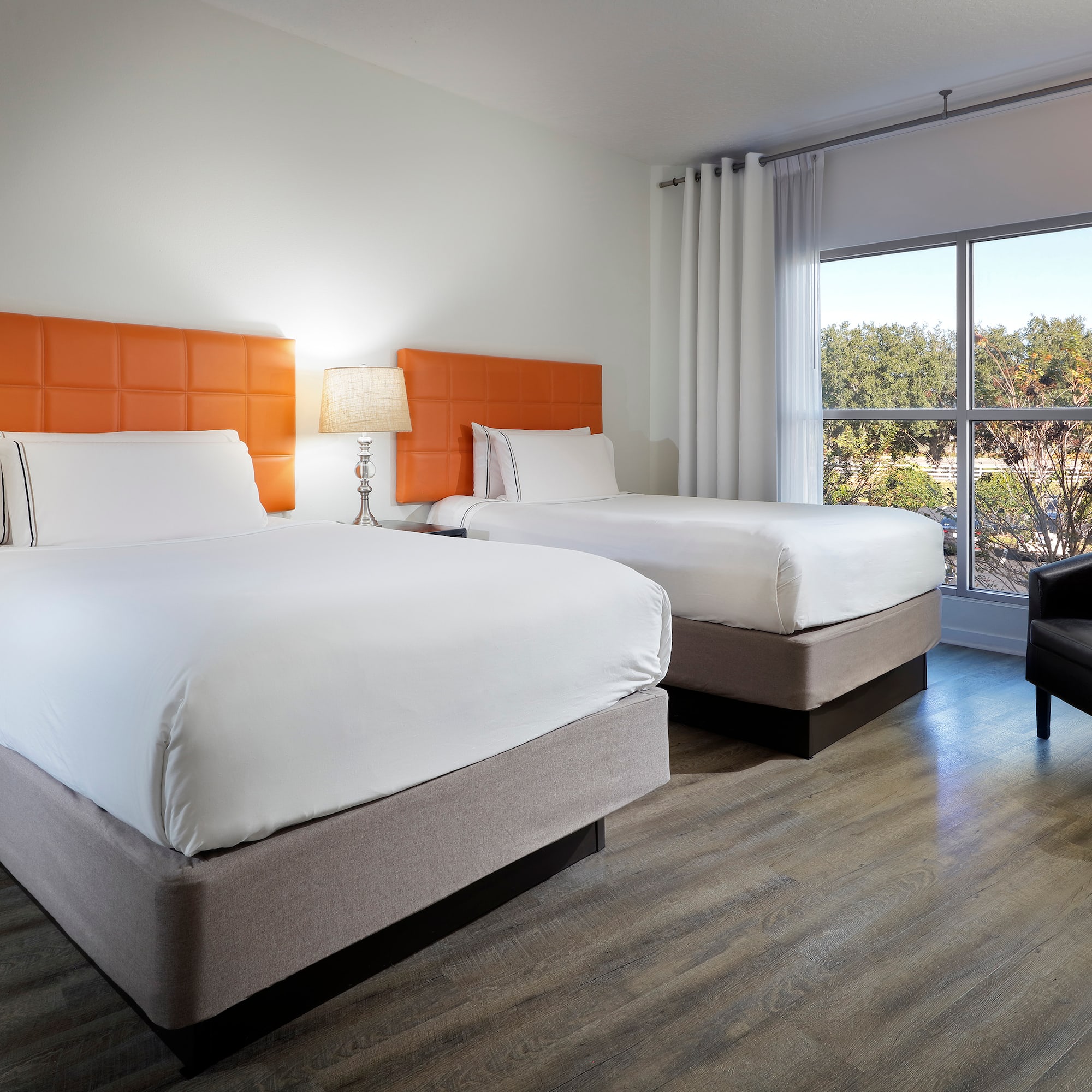 Hotel guest room with two double beds, orange headboards, window, armchair.