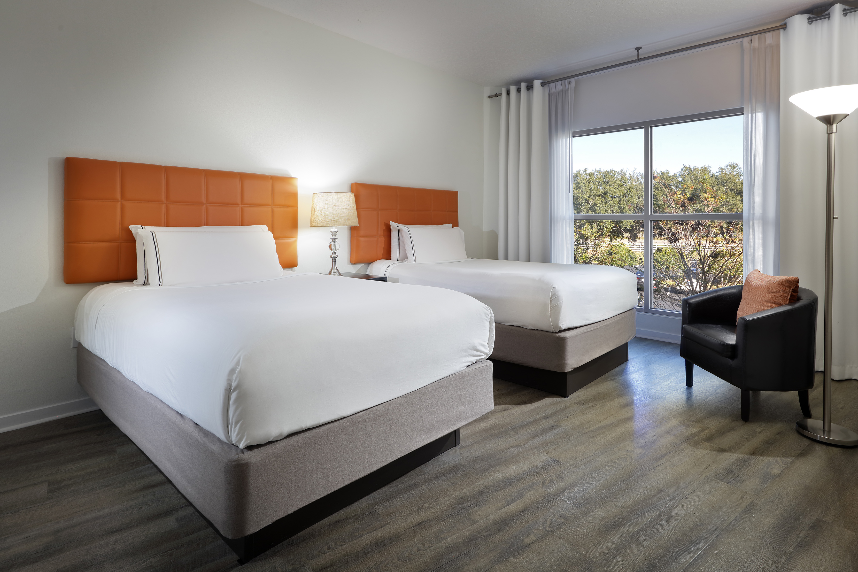 Hotel guest room with two double beds, orange headboards, window, armchair.